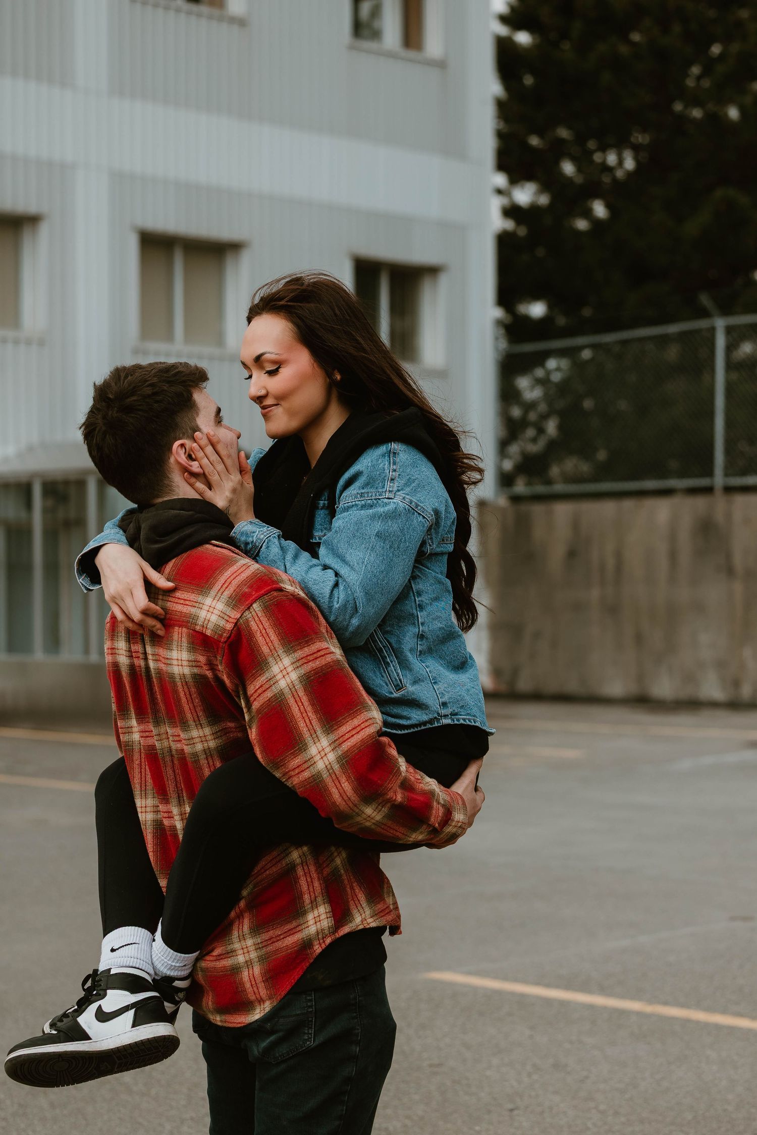 A romantic moment shared between a couple outside, with one person wearing a plaid shirt lifting the other in a denim jacket.