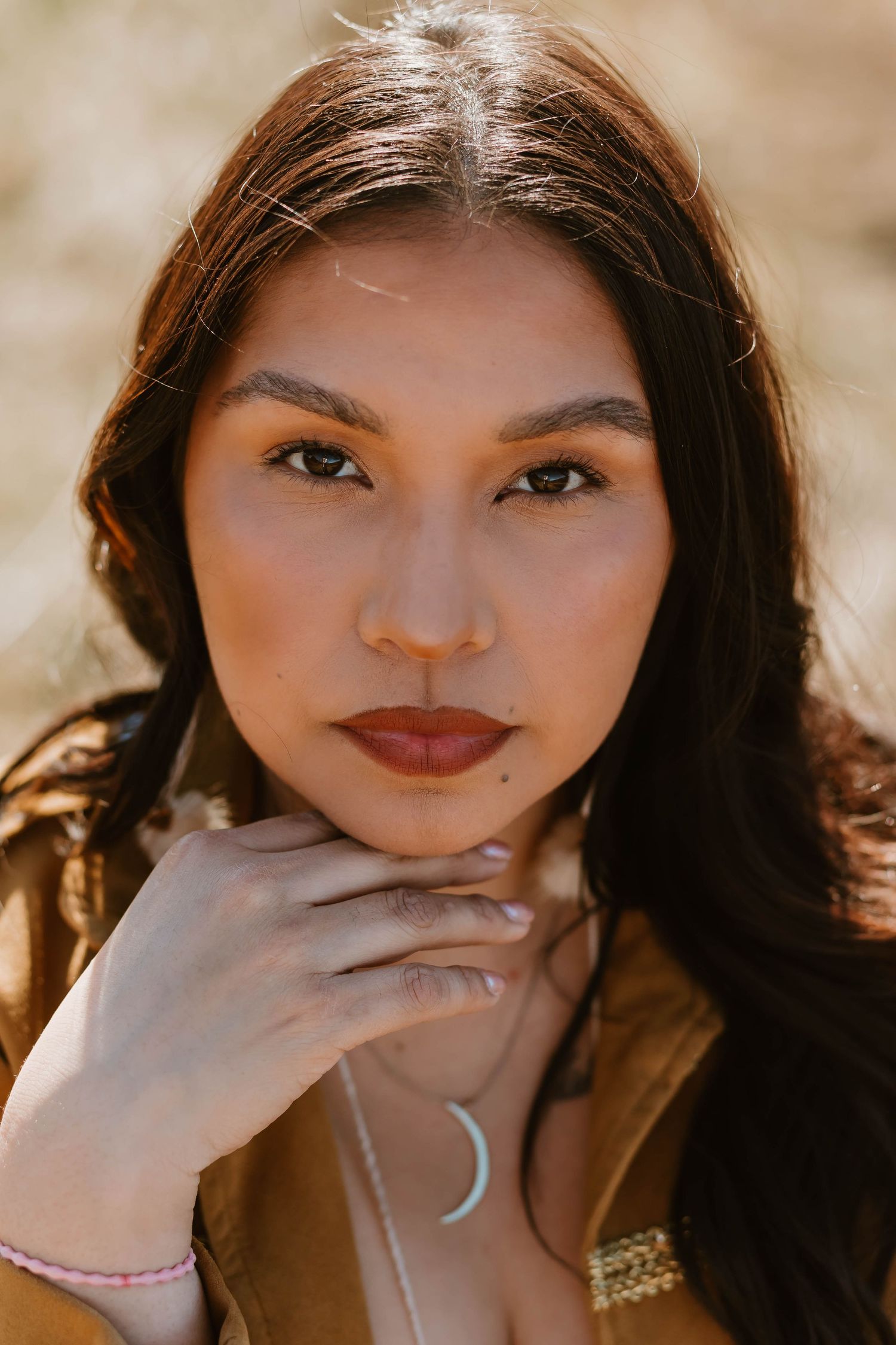 Portrait in warm sunlight showing dark hair, red lipstick, and delicate hand pose with crescent moon jewelry.