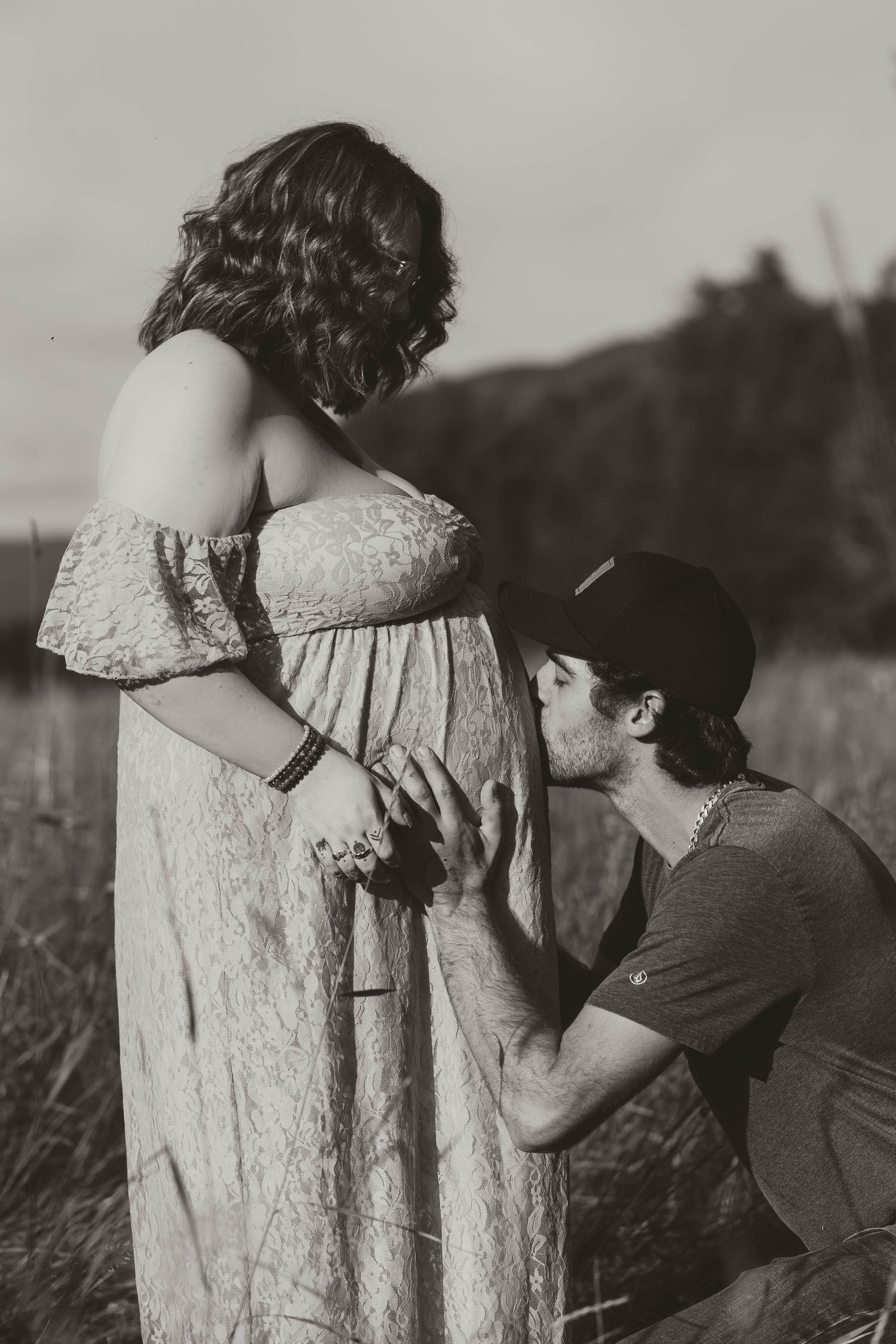 A black and white maternity photo showing an intimate moment in a field.
