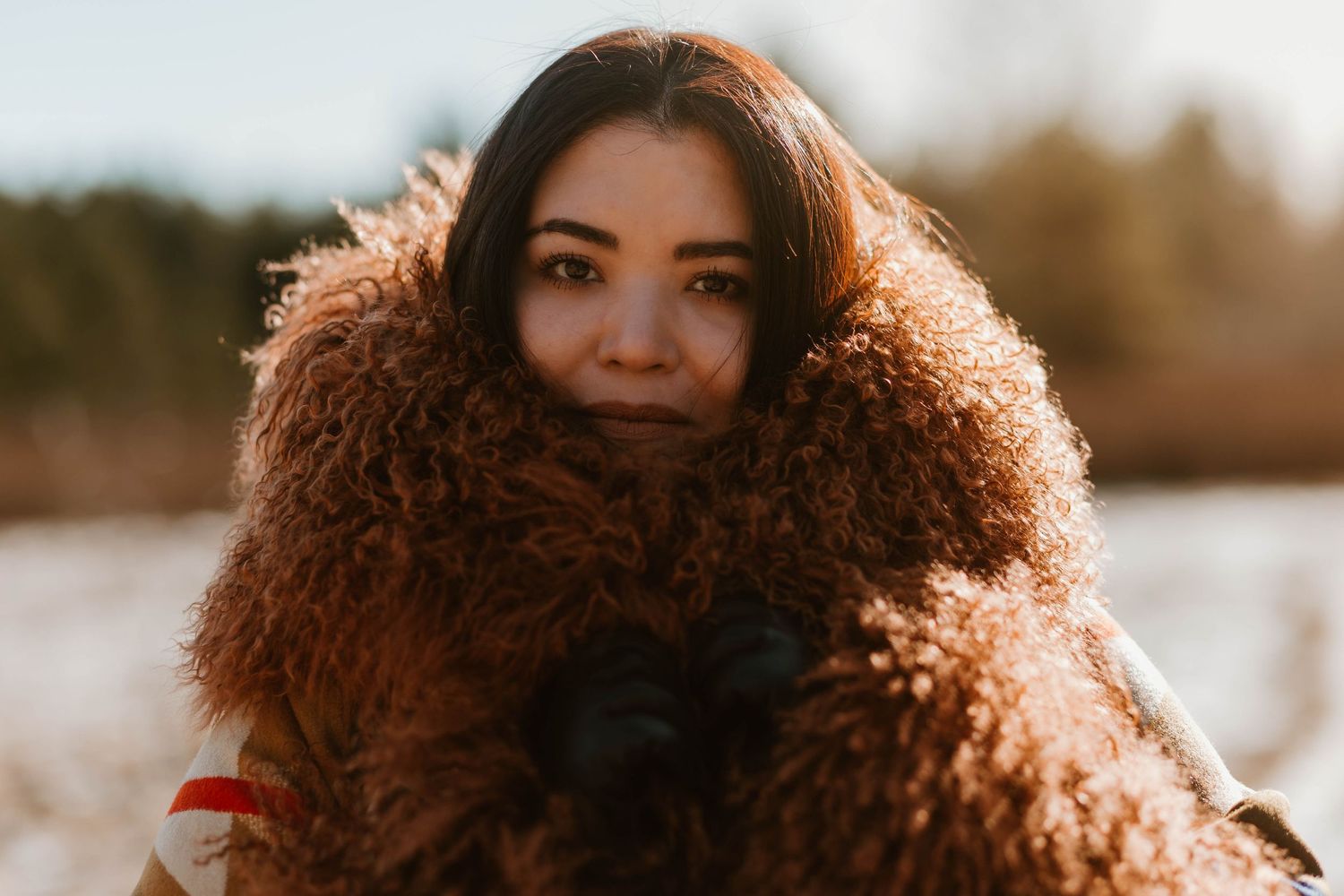 Person wrapped in fluffy brown fur coat during golden hour sunset.