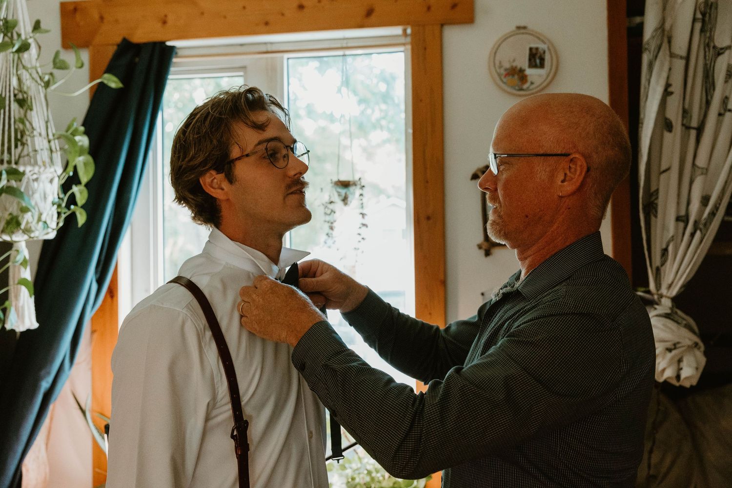 Two people sharing a moment while adjusting formal attire indoors.