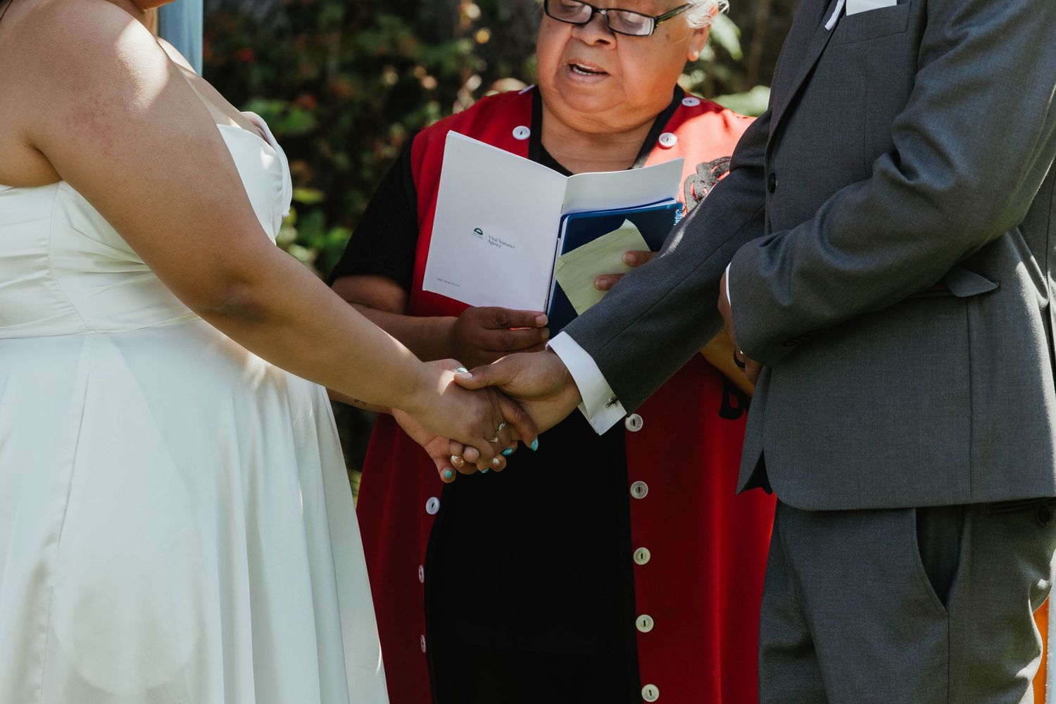 Close up of hands clasped during wedding ceremony with officiant in red holding a book.