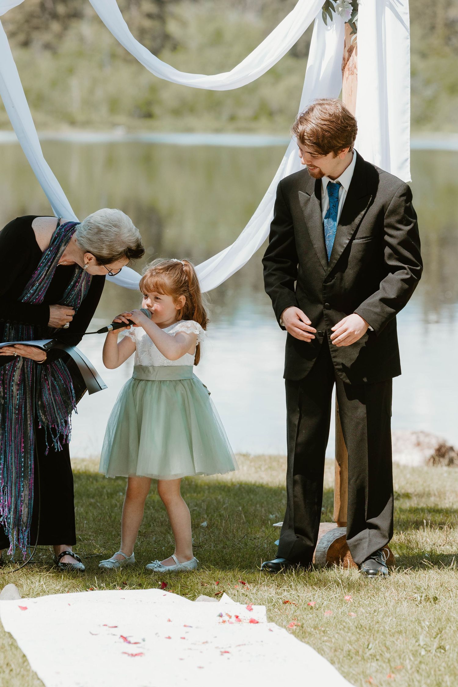 Sweet moment during wedding ceremony as young flower girl interacts with guests by white arch.