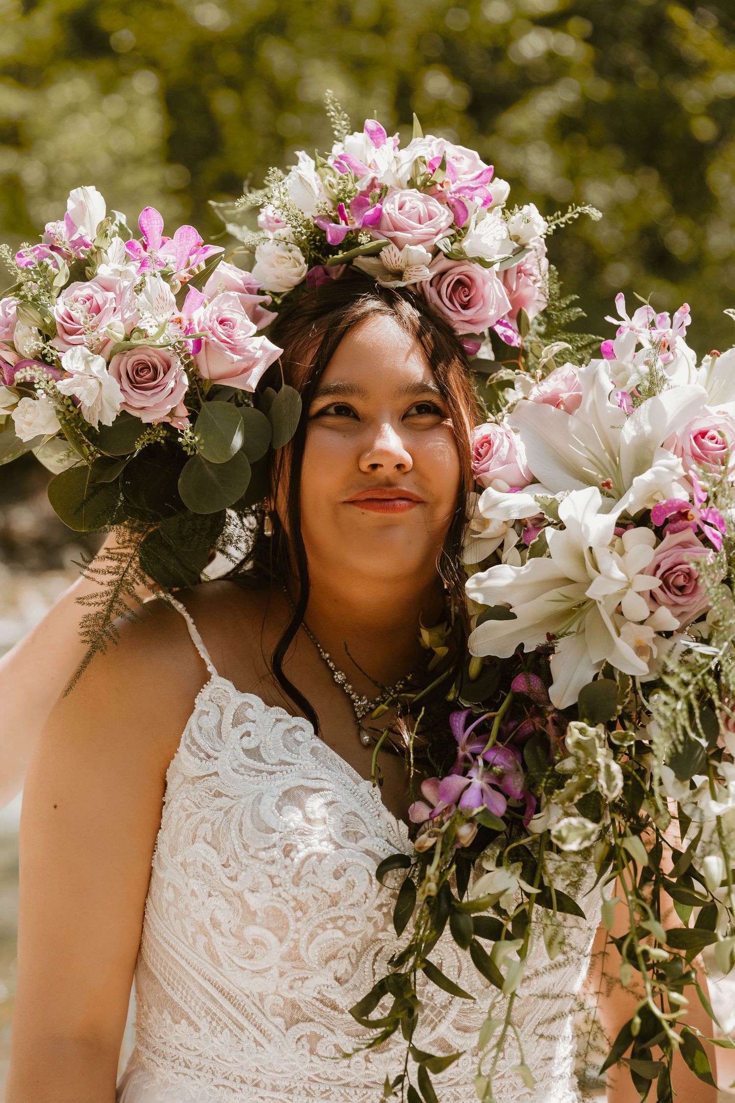 Bride wearing a floral crown and lace dress holding a pink and white rose bouquet.