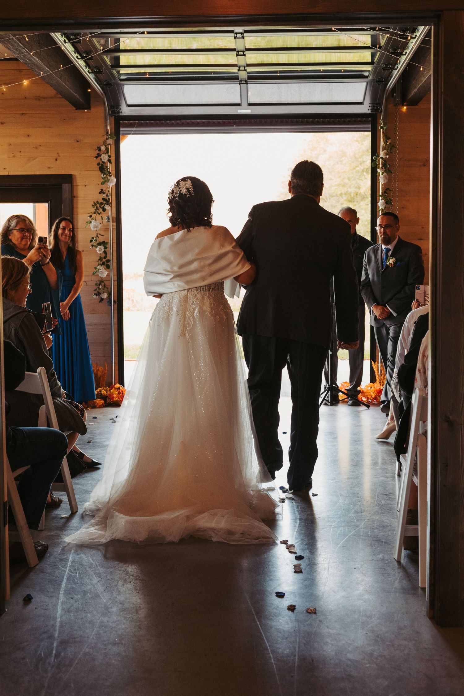 Wedding couple silhouetted in doorway walking through guests at indoor venue.
