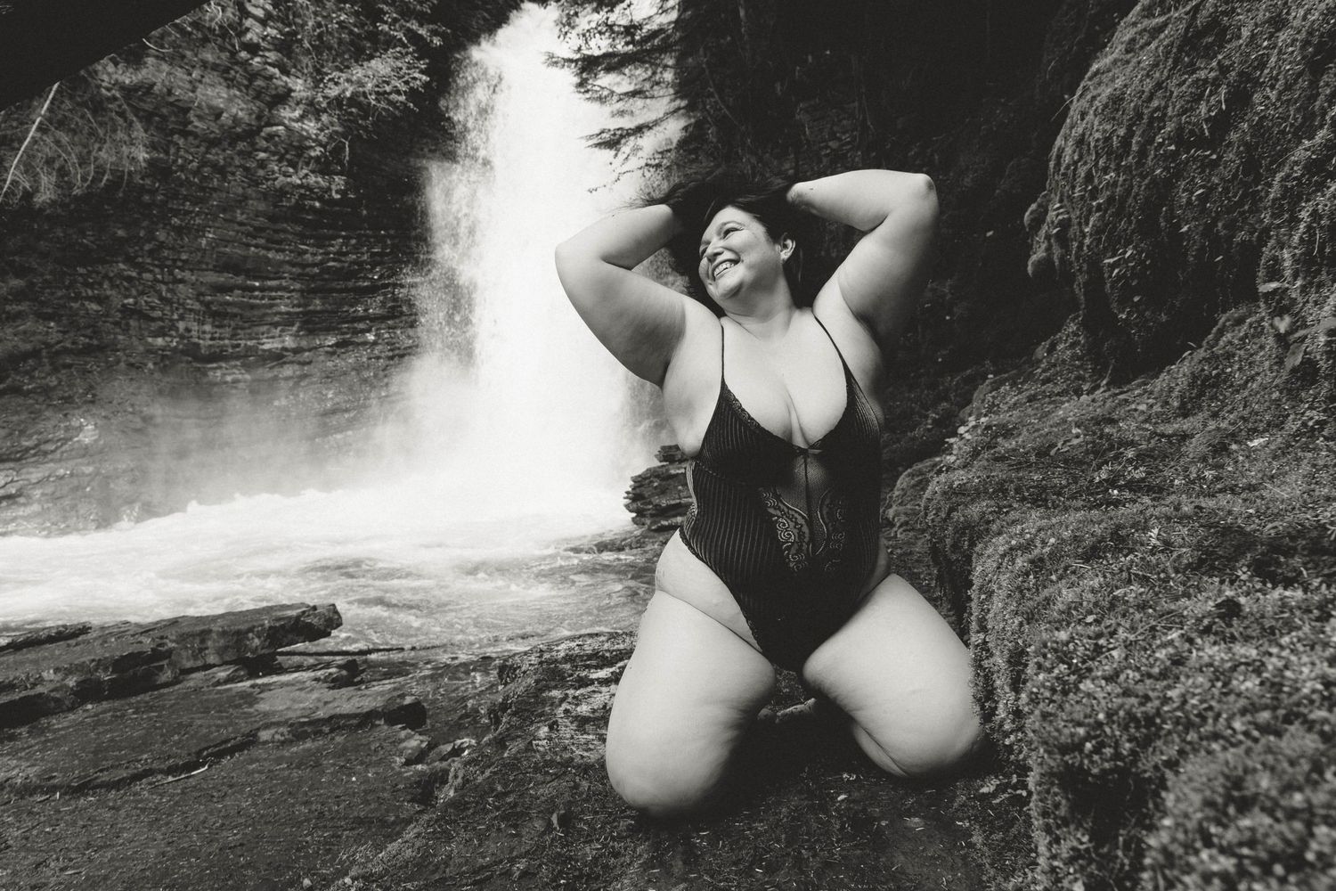 Black and white portrait of person posing by waterfall wearing swimsuit.