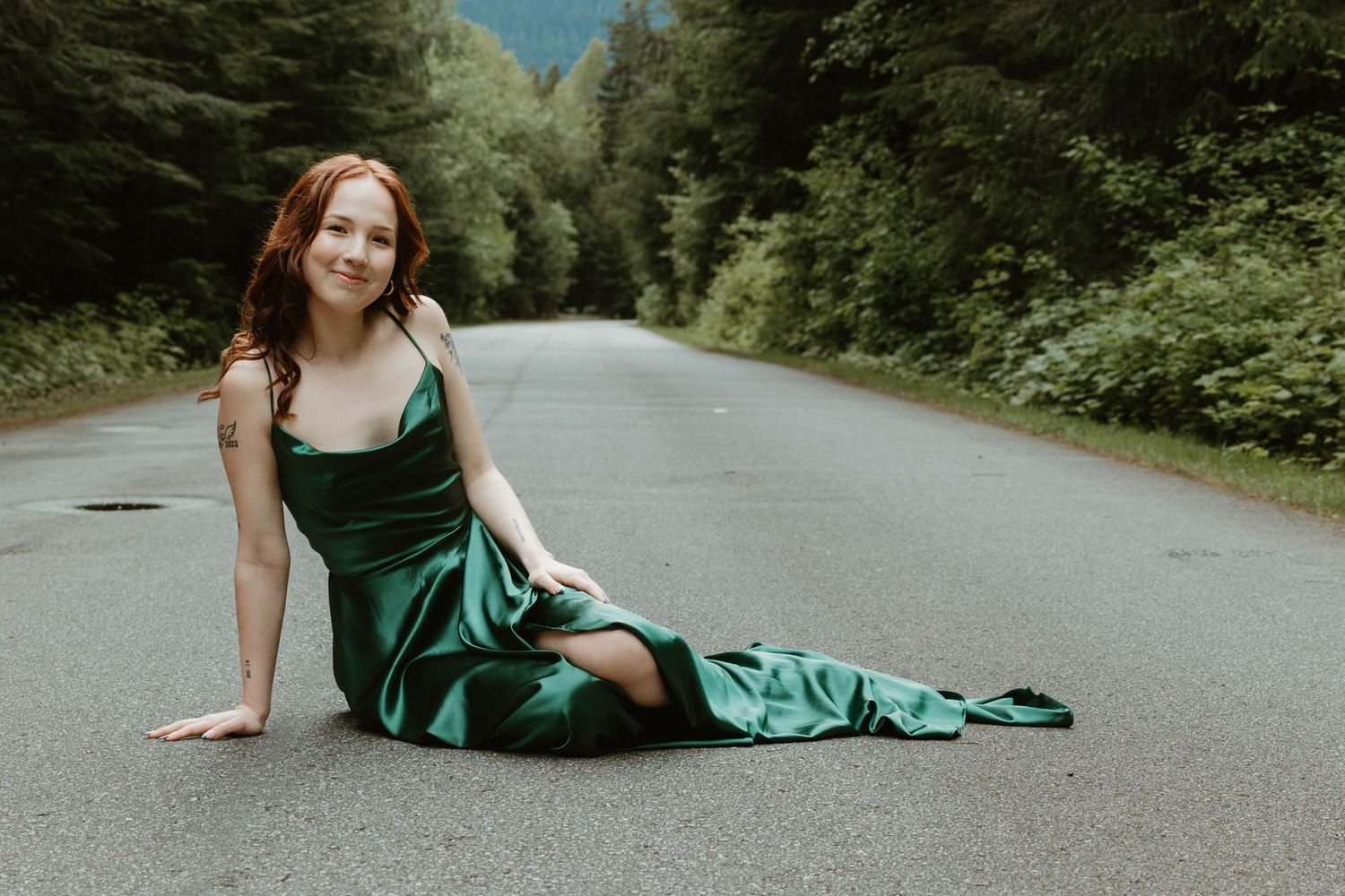 Elegant portrait on empty forest road in flowing emerald evening gown.