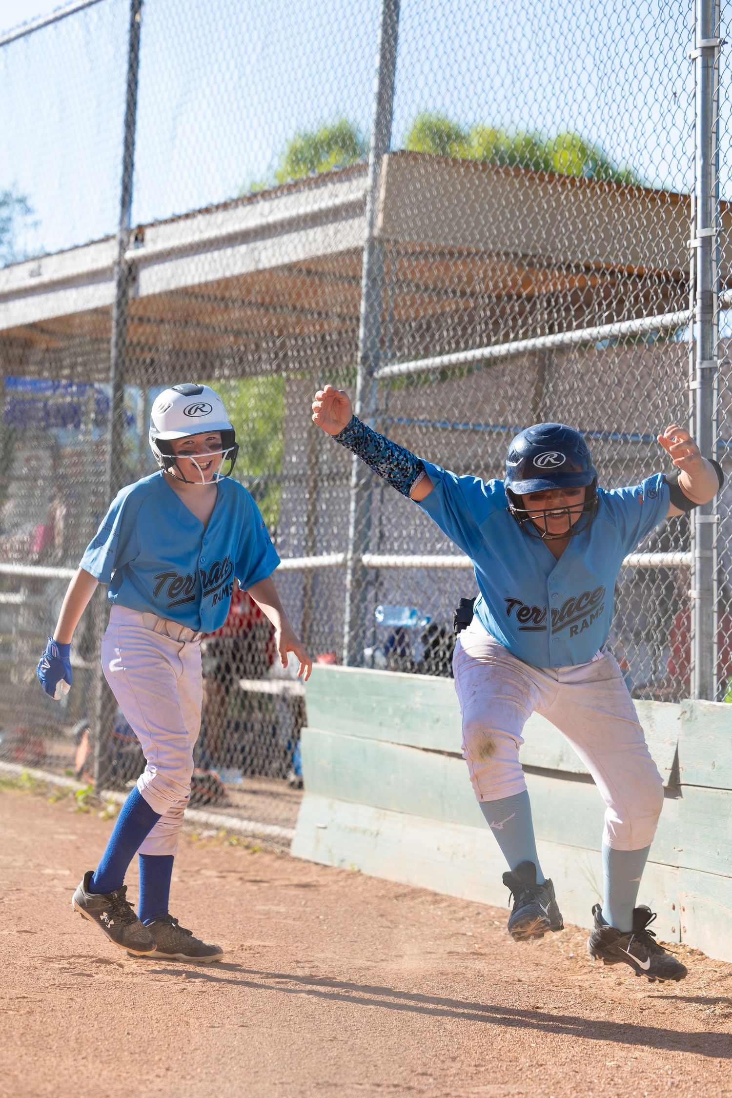 Two baseball players in blue uniforms celebrate on the basepath during game.