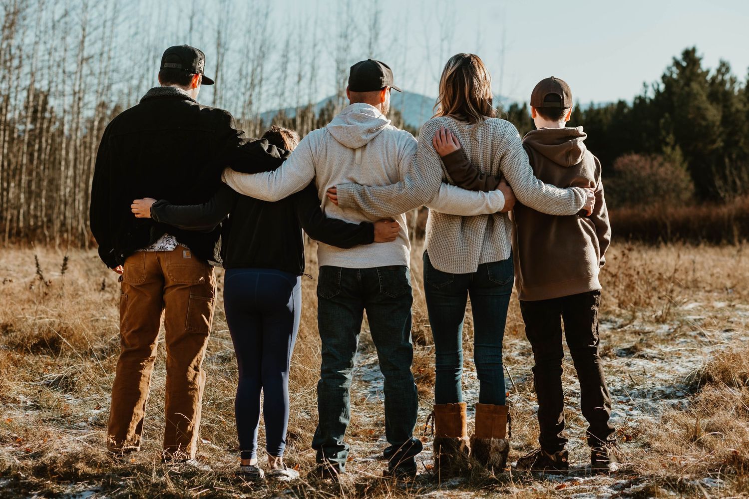 A family stands with arms around each other looking at mountain views.