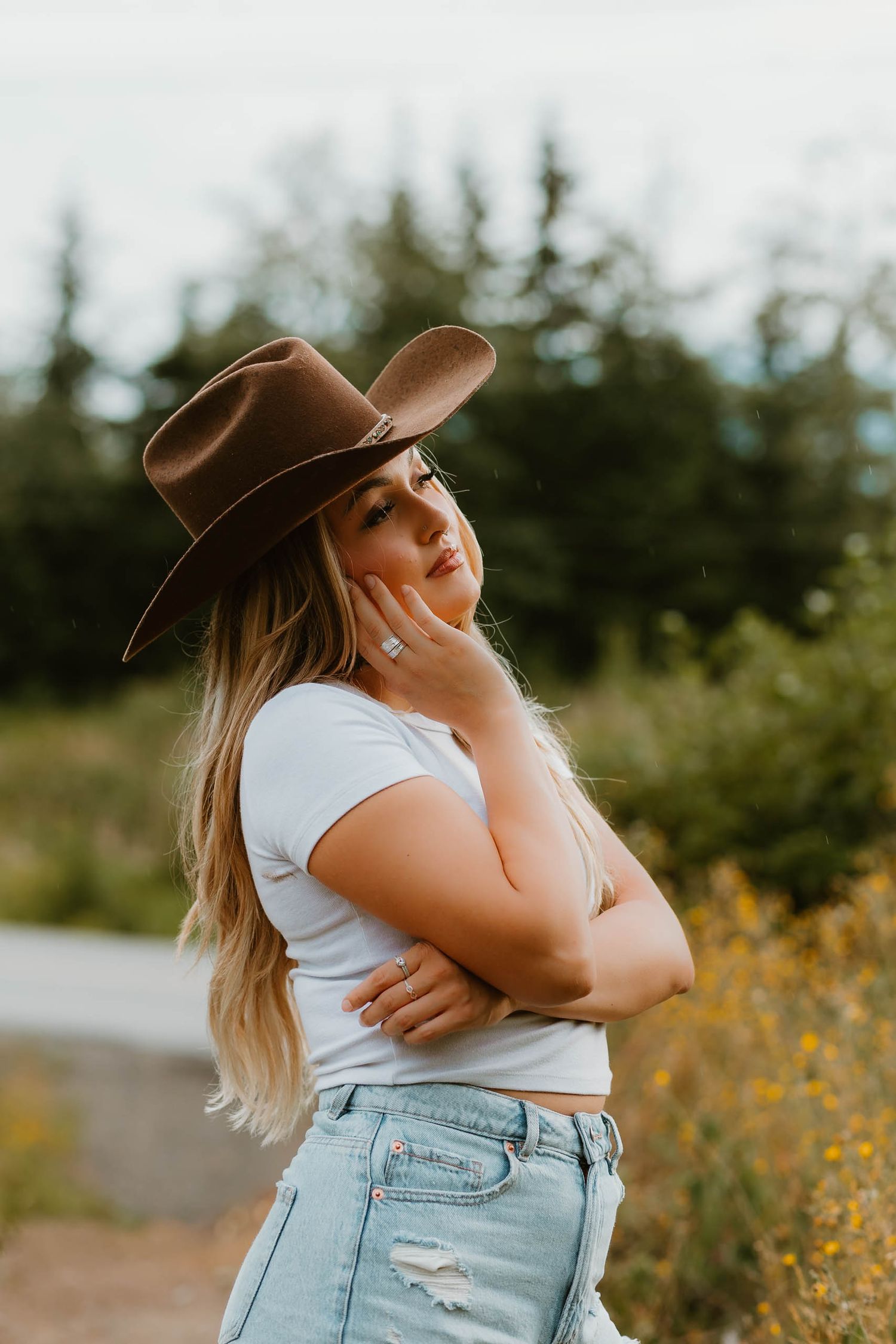 Person in casual attire and brown cowboy hat poses against natural backdrop.