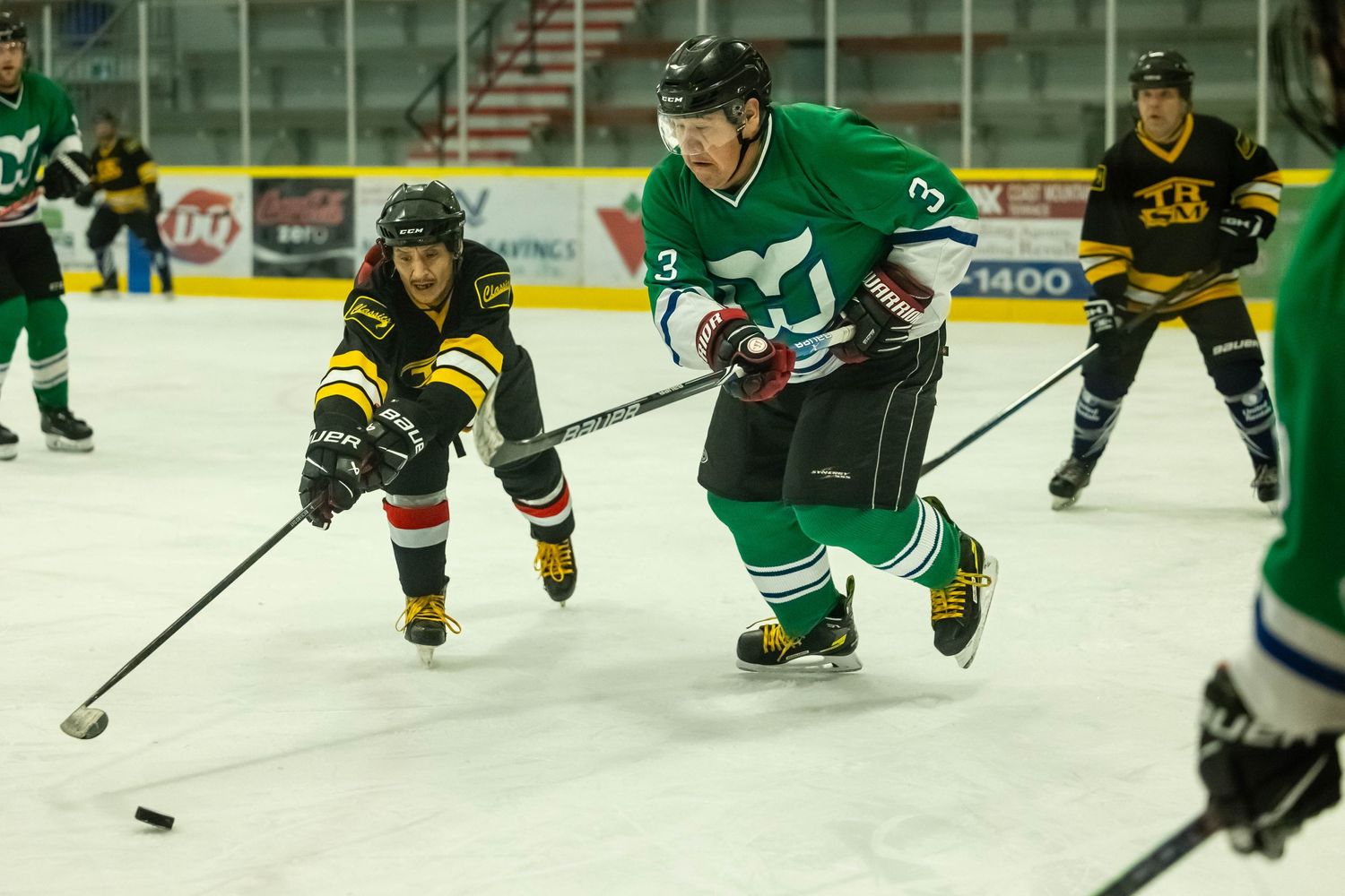 Hockey player in green jersey controls the puck while opponent in black and yellow follows.