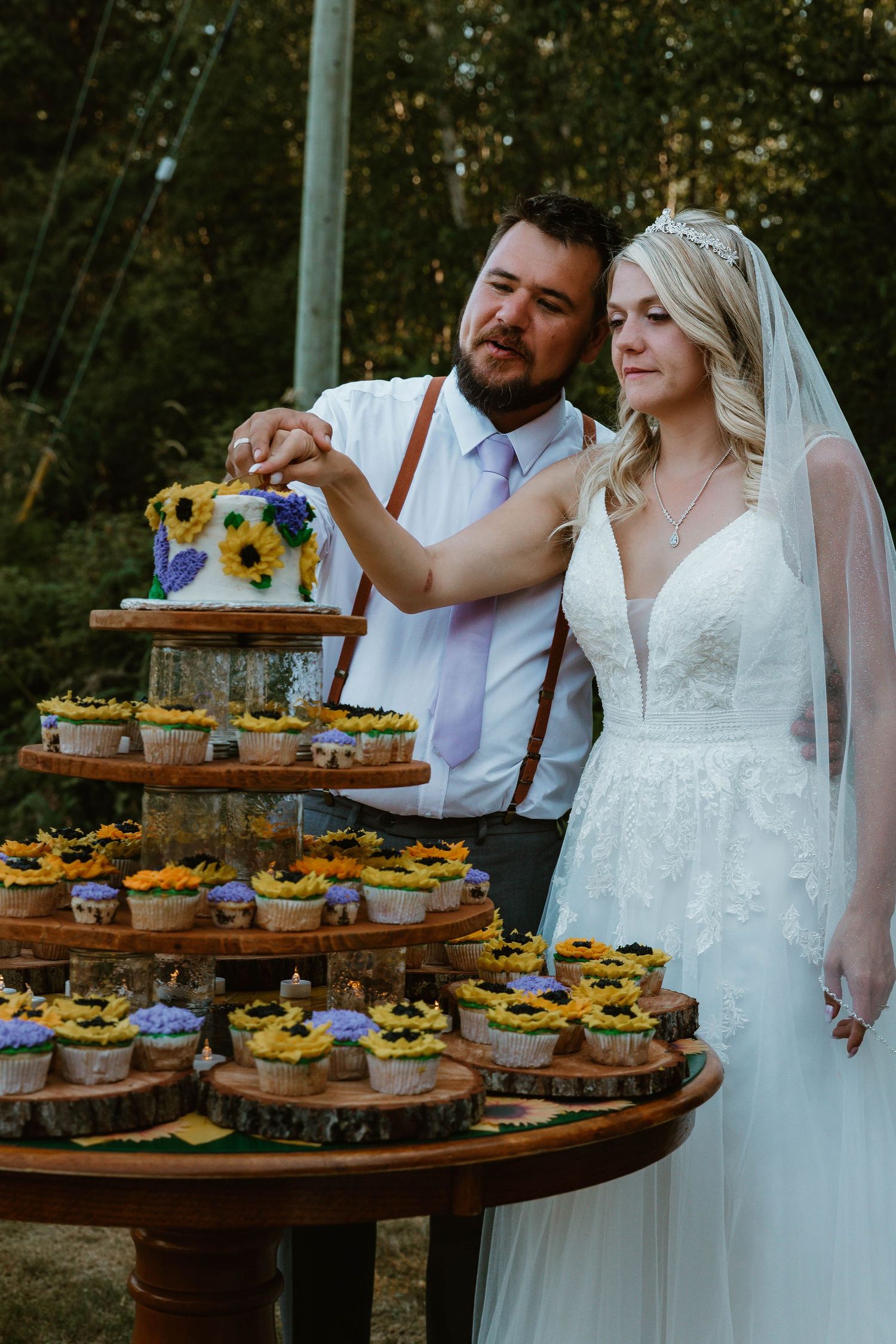 Couple cutting their sunflower-decorated wedding cake display on rustic wooden stands.