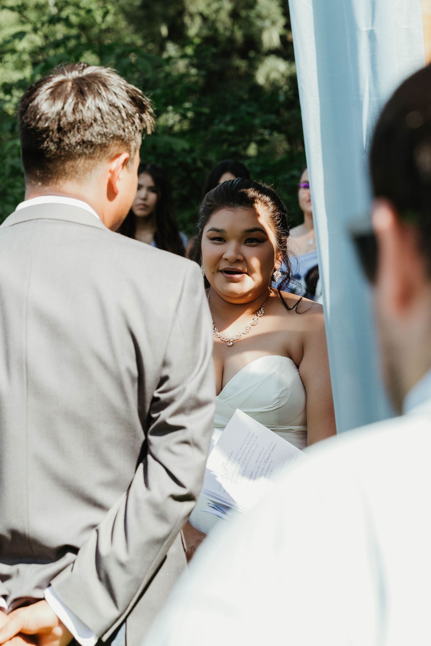 An intimate moment during a wedding ceremony under a light blue arch with lush greenery in the background.