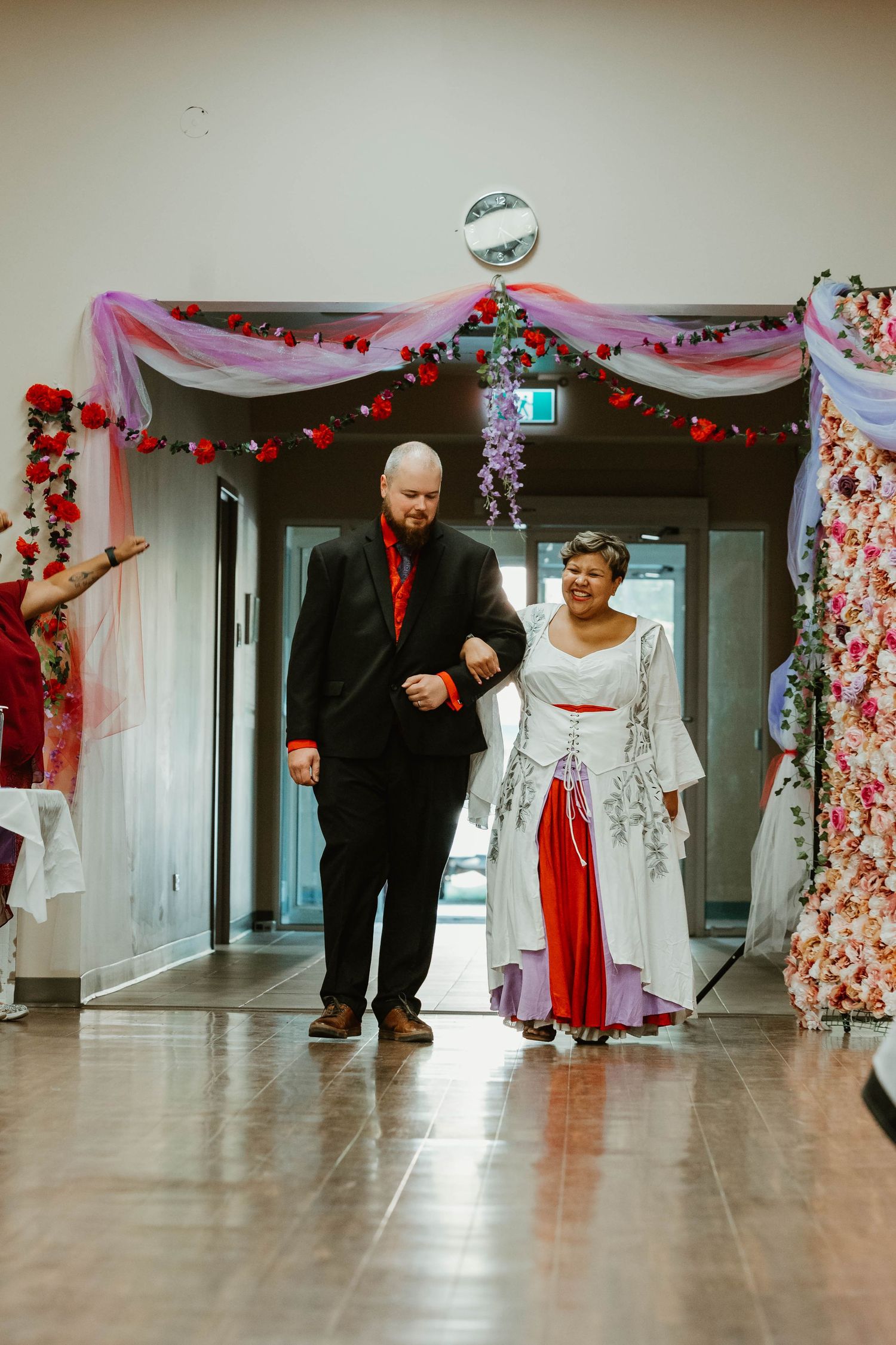 A couple walking down a hallway decorated with pink drapes and red heart lights for a celebration.