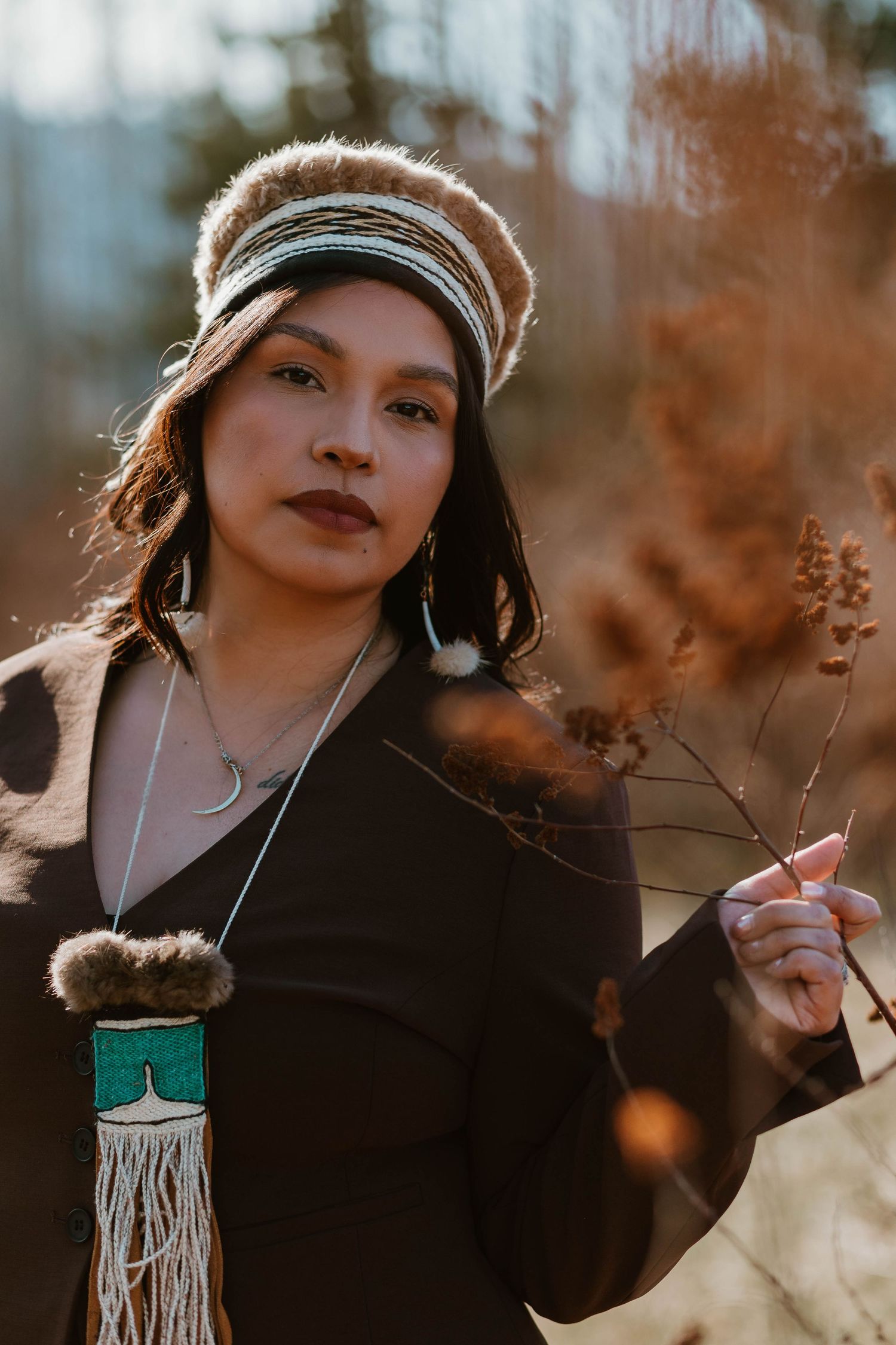 Winter portrait at golden hour featuring a person in a knit cap and black top holding traditional Indigenous crafts.