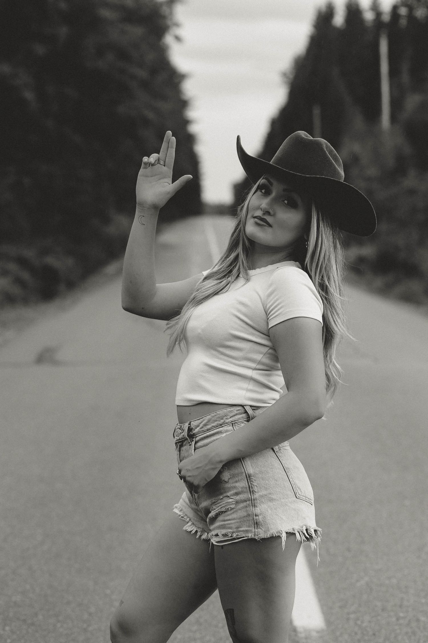 Black and white portrait of person in cowboy hat posing on rural road.