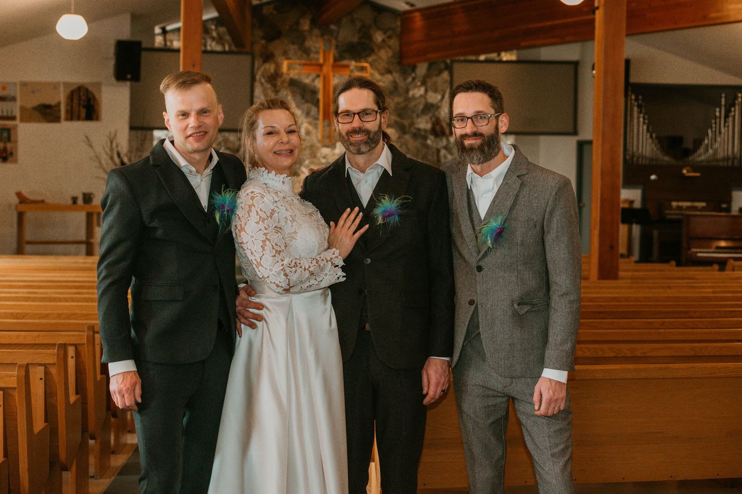 Wedding party poses together in church interior with wooden pews and stone wall backdrop.