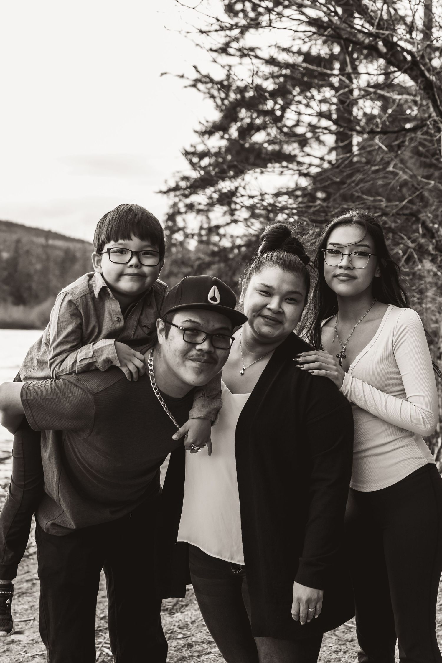 Group poses together outdoors for casual portrait by evergreen trees and water.