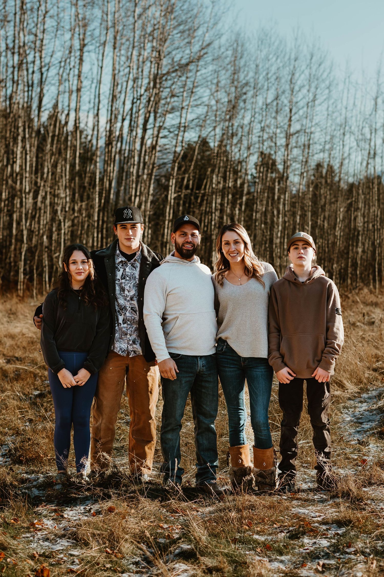 A family of five stands together for a portrait in front of bare winter trees.