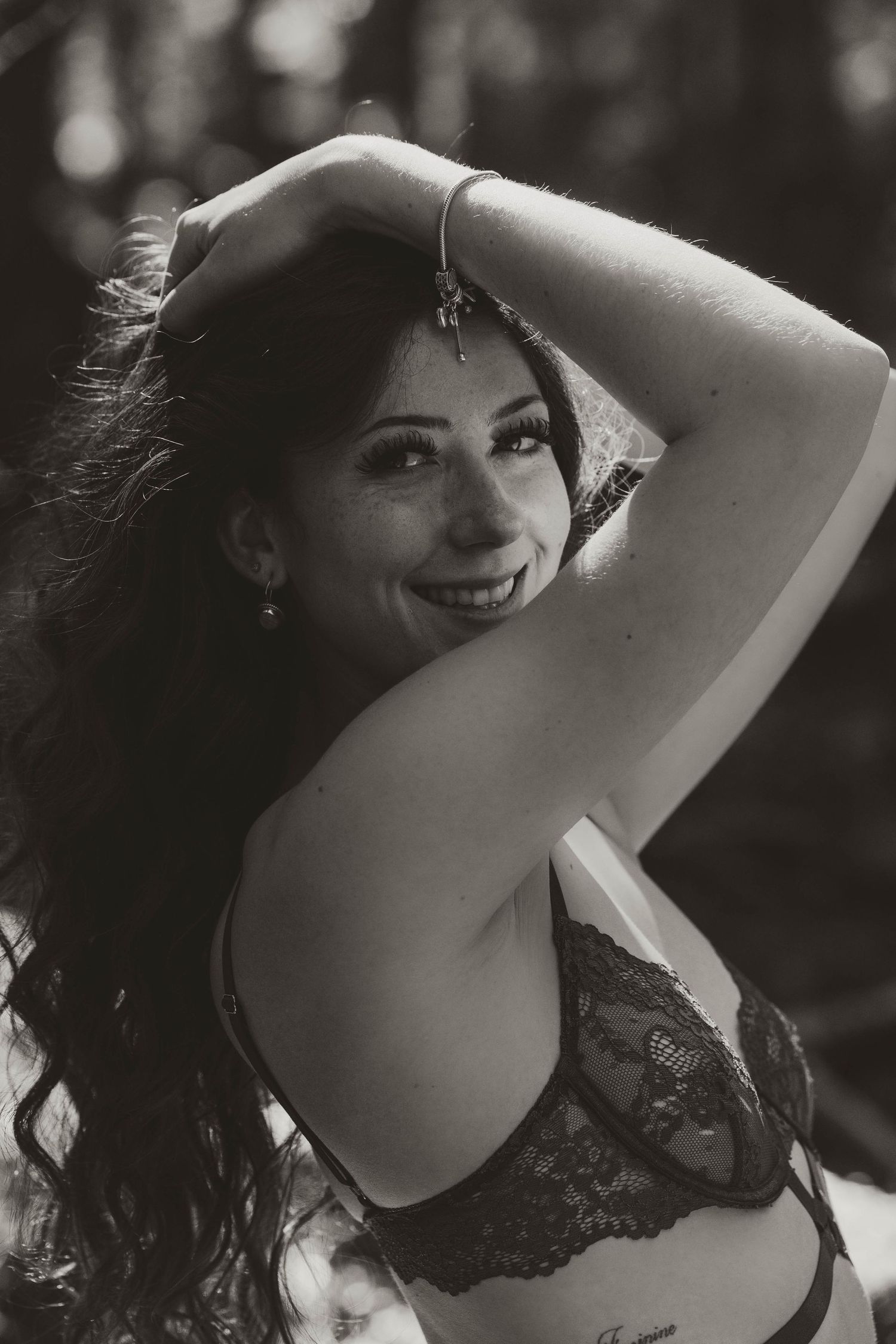 Vintage-style black and white portrait in lace lingerie against forest backdrop.