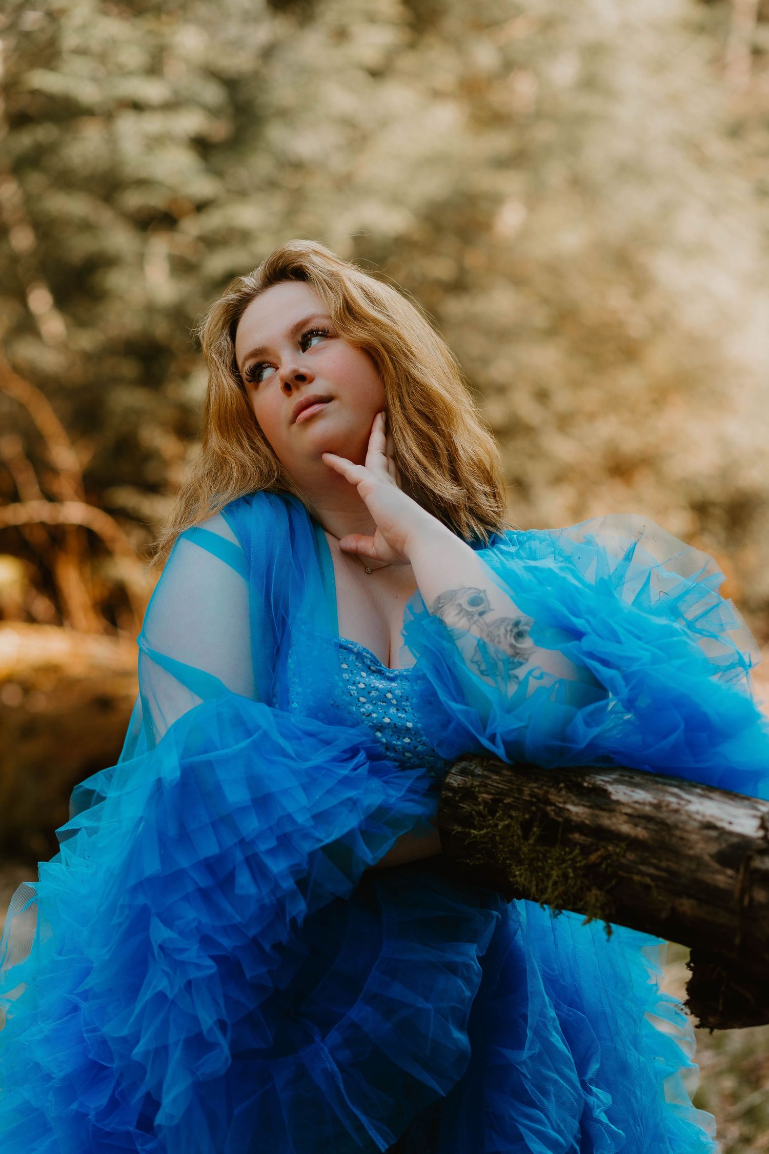 A dreamy portrait in a vibrant blue tulle gown against a warm autumn forest background.