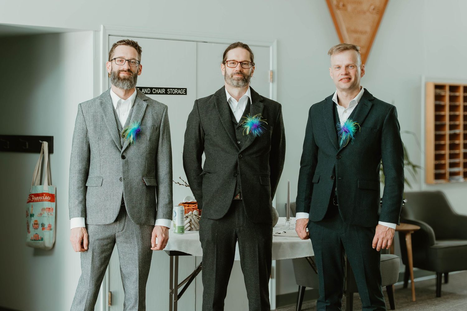 Three people in formal suits with matching teal accessories stand together indoors.