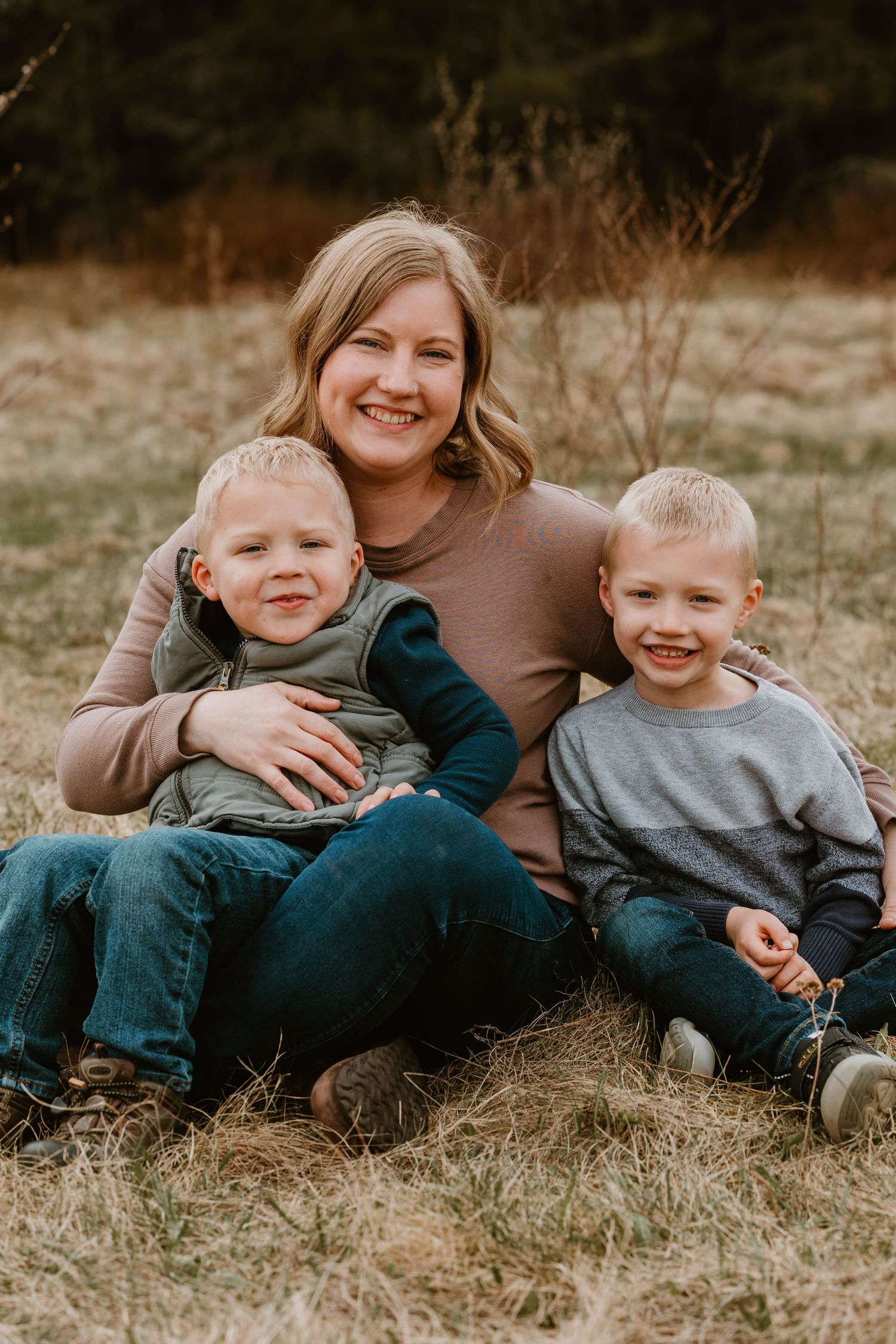 Casual family portrait on grass with evergreen trees in background.