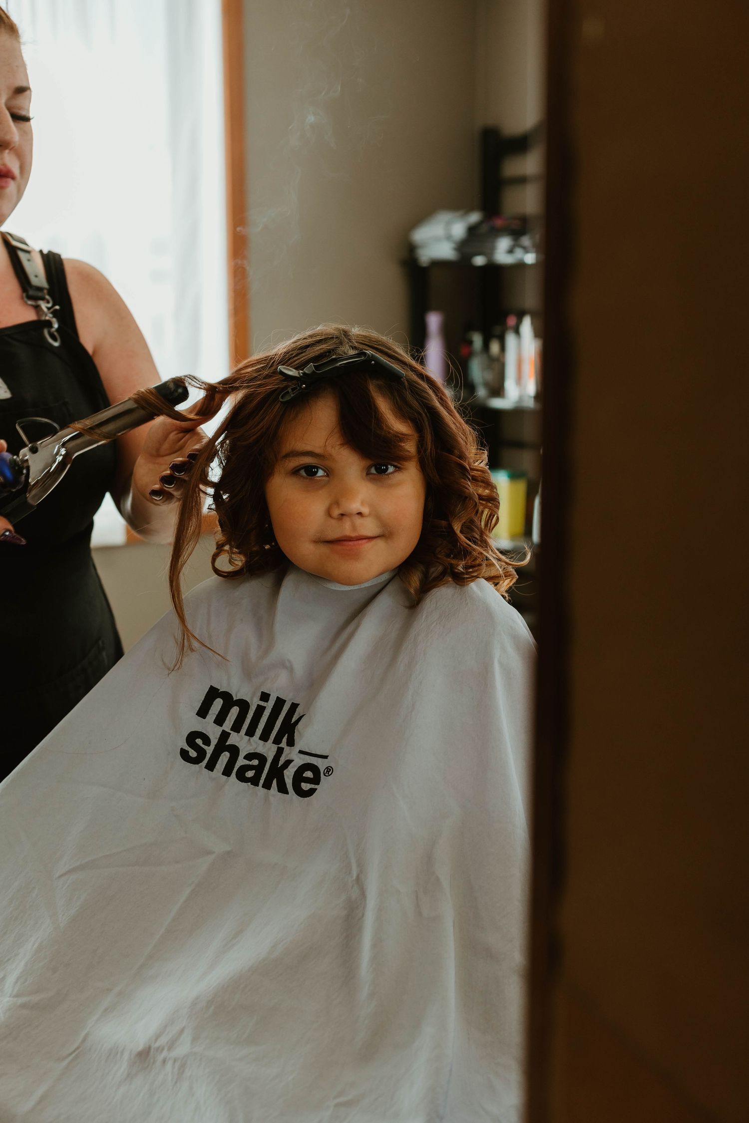 Young person getting hair styled while wearing a white Milk Shake branded salon cape.