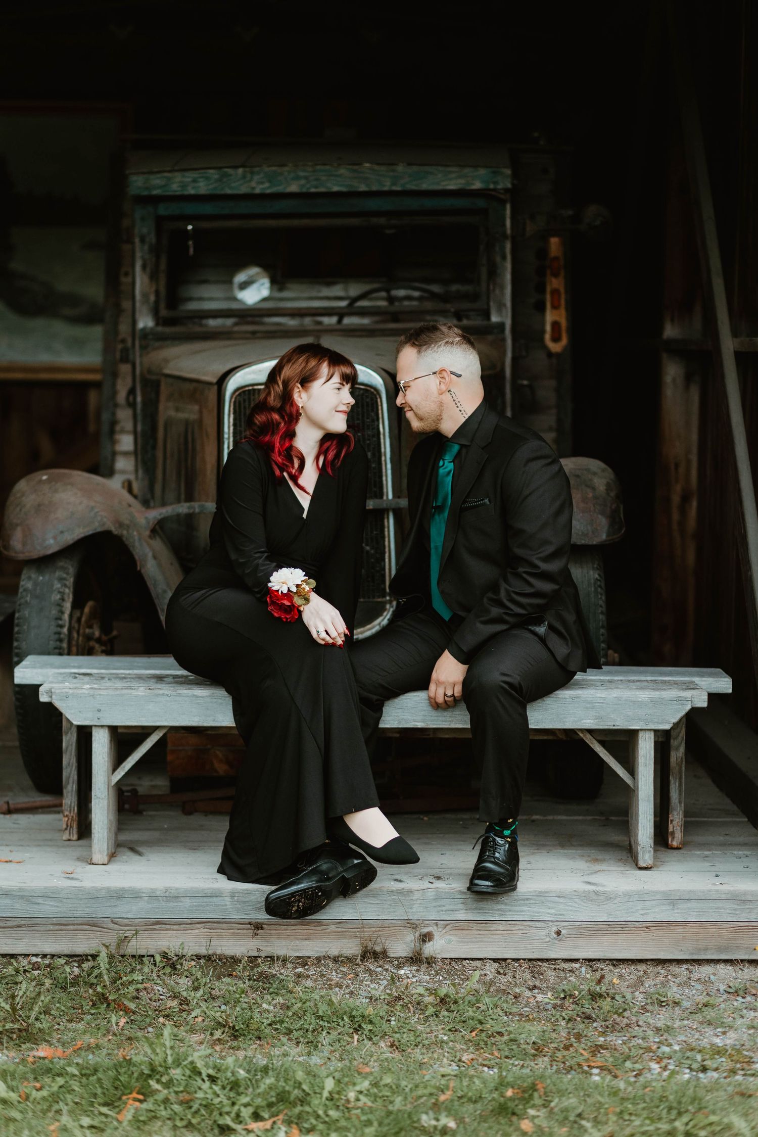 A couple in formal attire sitting together on a rustic wooden bench.