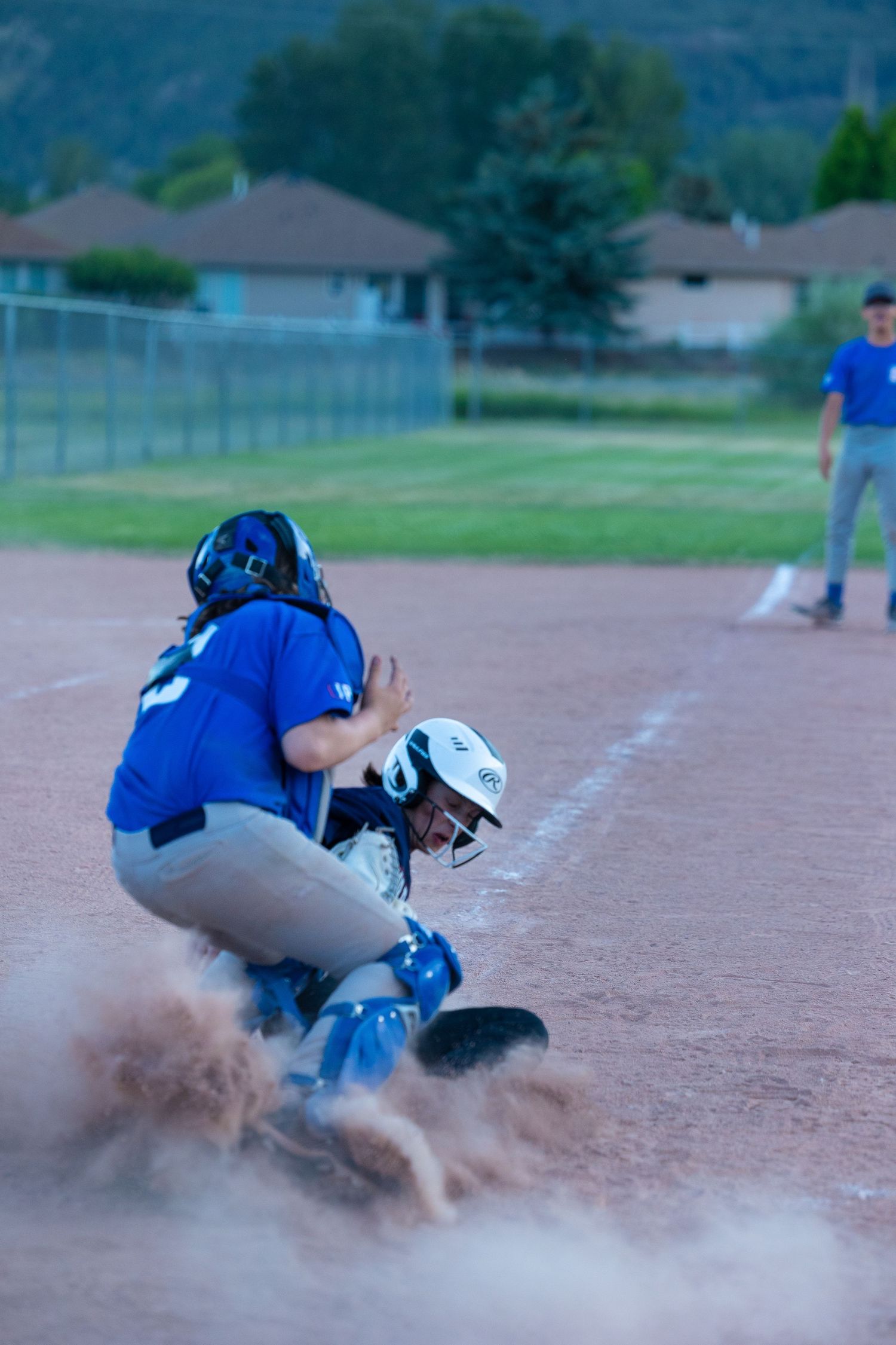 Baseball catcher crouching at home plate in blue uniform as dust flies during game action.