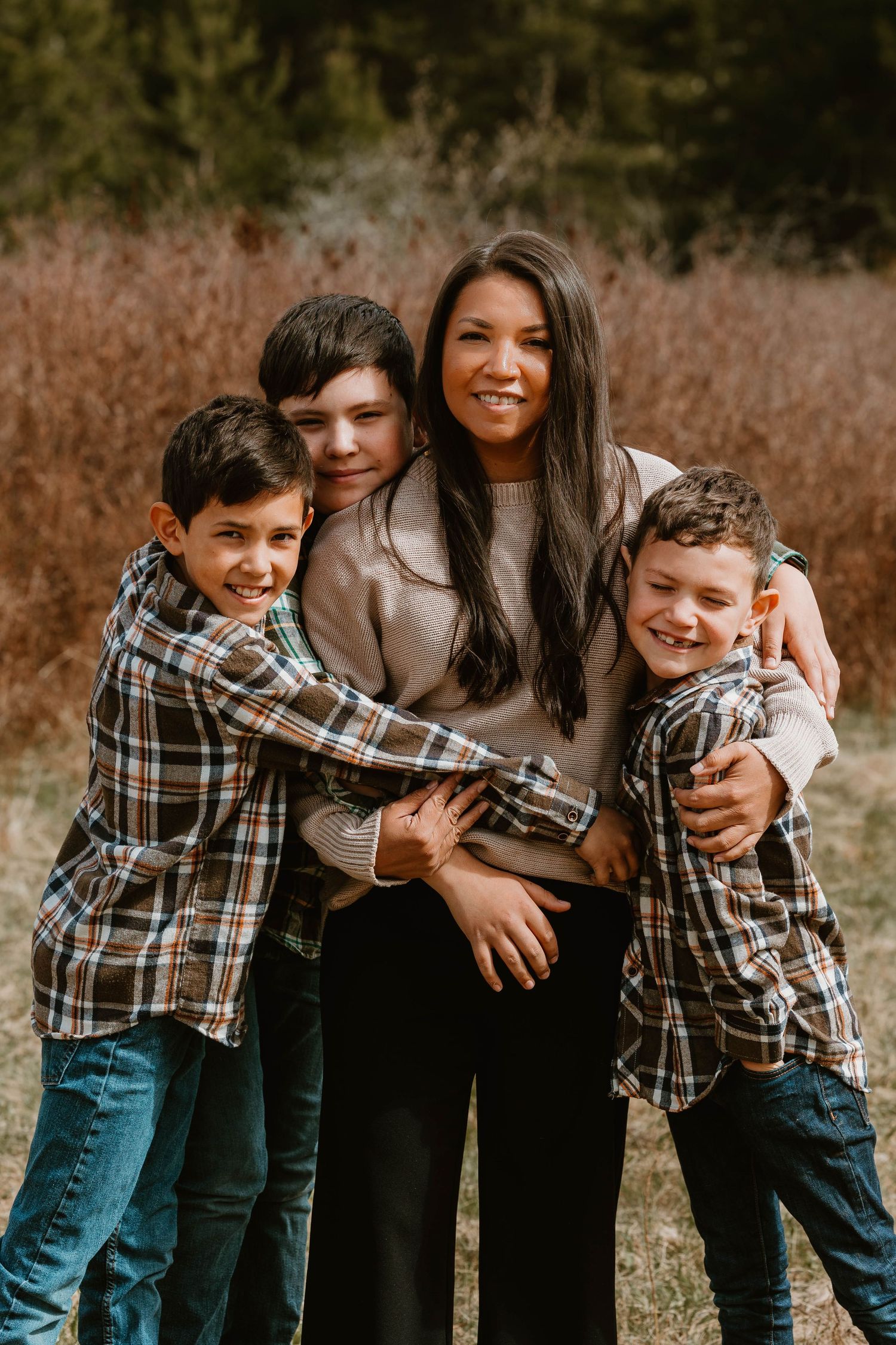 A warm family embrace outdoors with coordinating plaid shirts against a natural background.