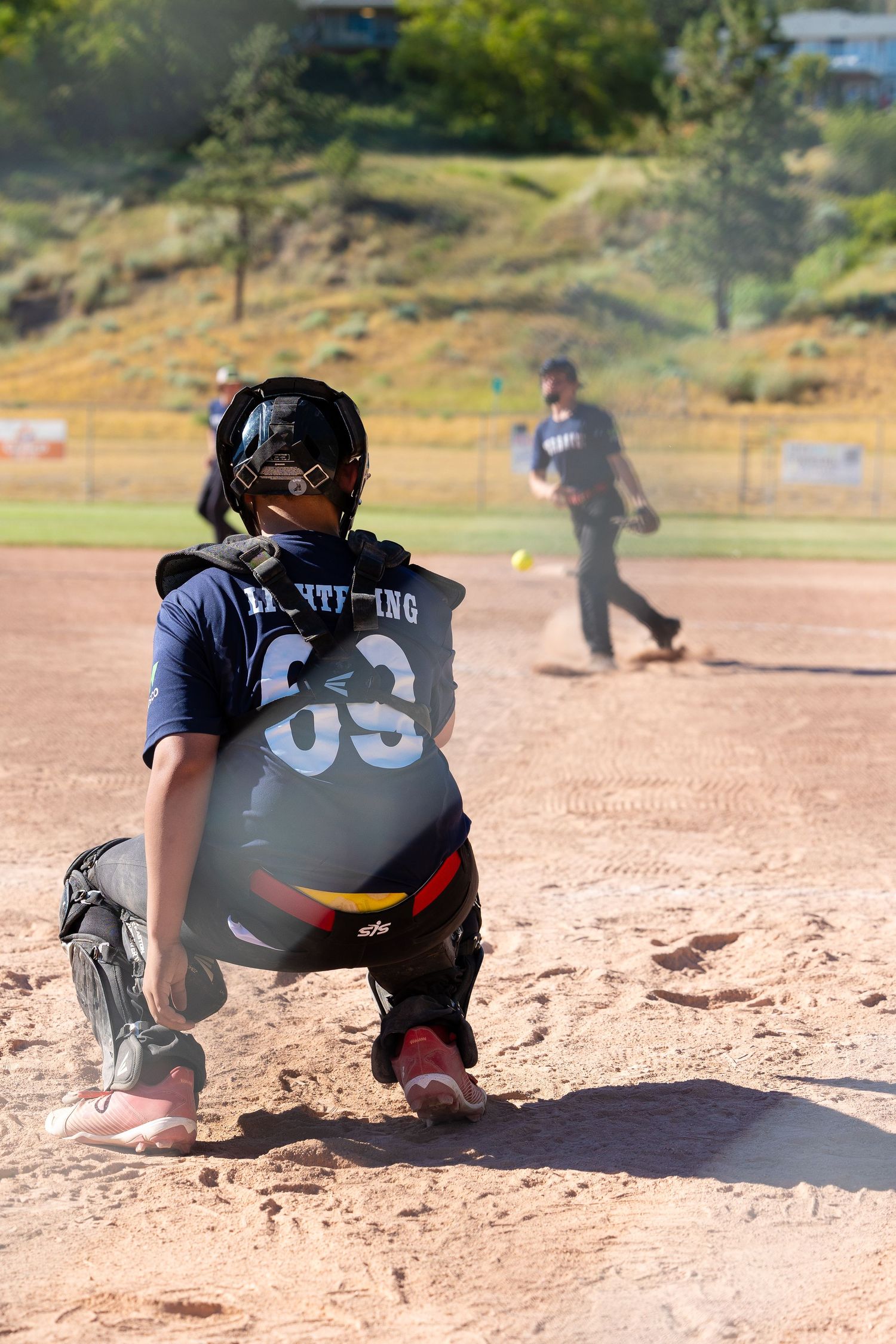 Youth baseball catcher in navy uniform crouches behind home plate during game.