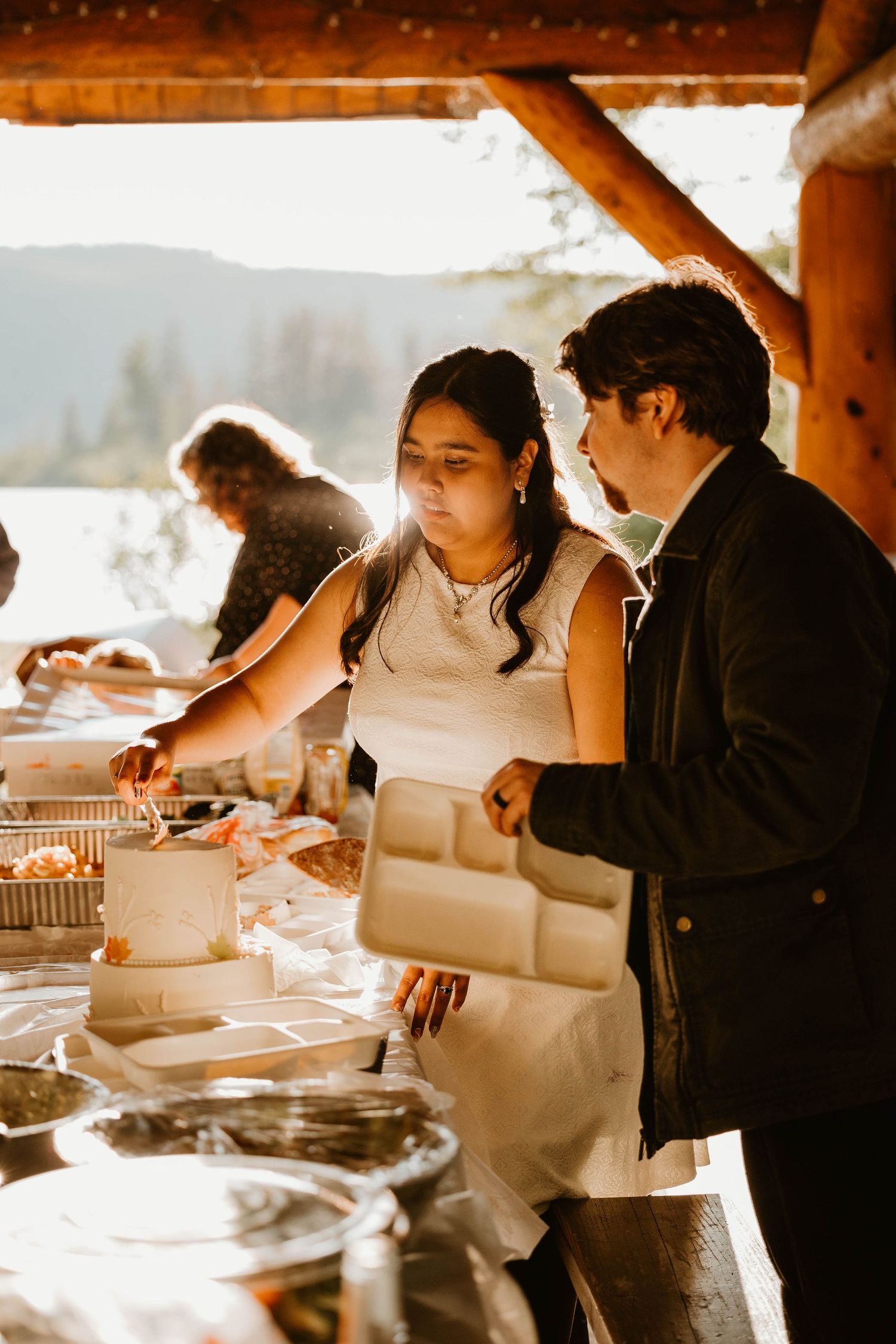 A wedding reception buffet line under a covered outdoor venue with golden sunlight.