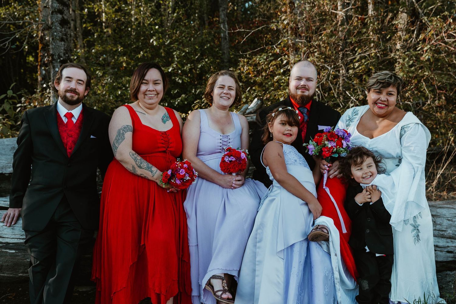 Wedding party in red and lavender attire poses together outdoors.