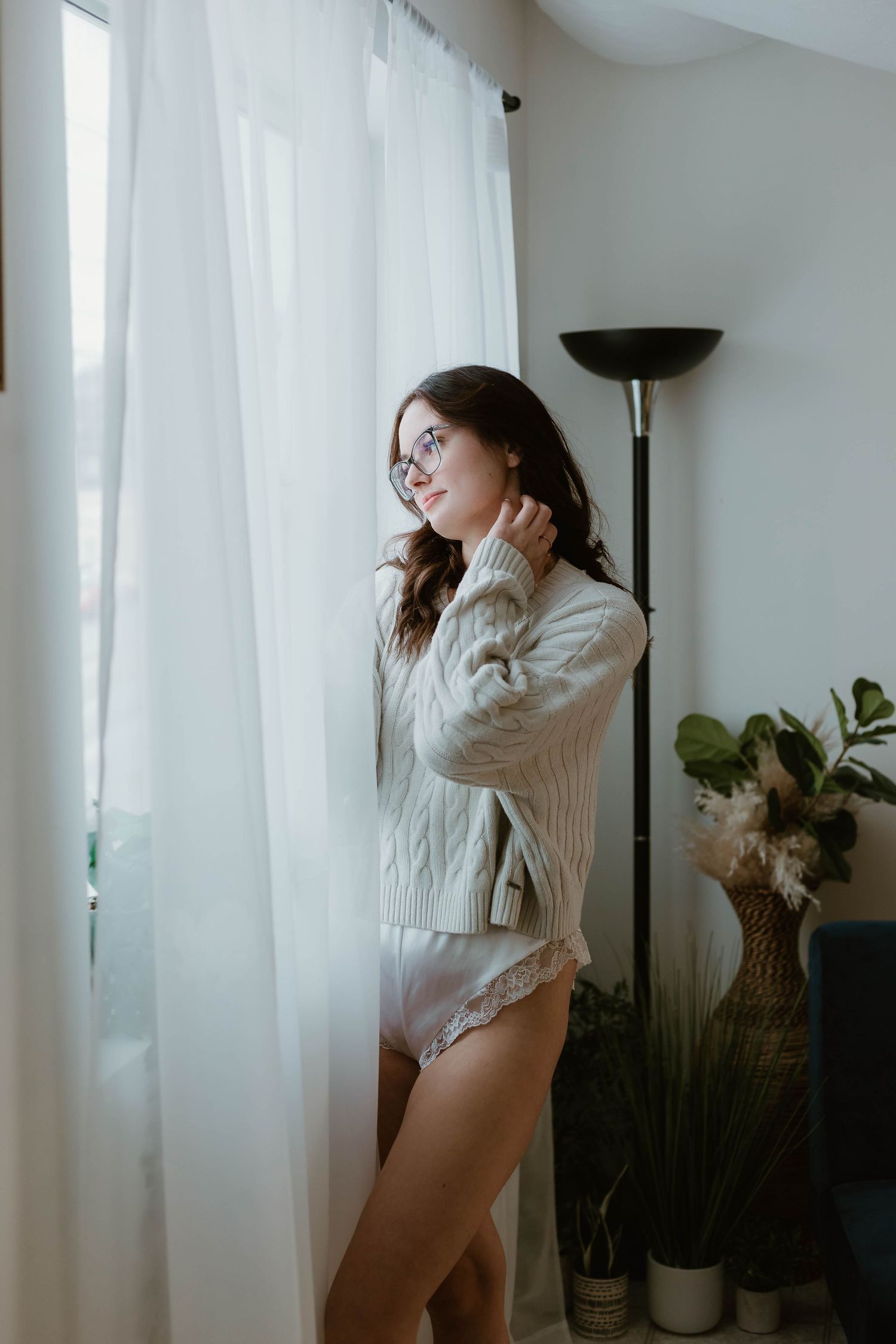 Person in cream sweater by window in sunlit room with indoor plants.