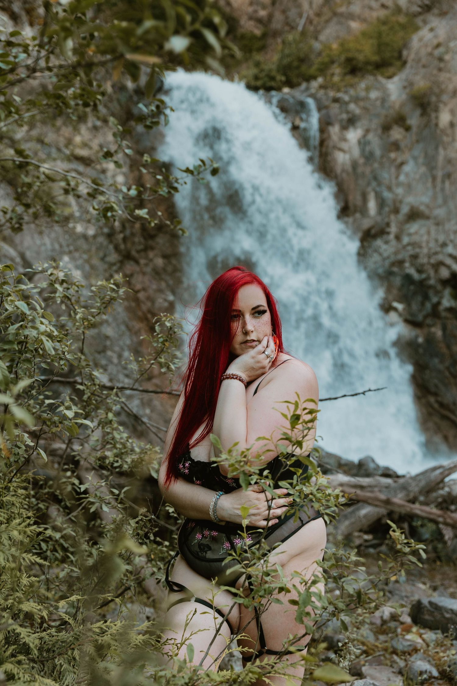 Person with red hair in dark attire near cascading waterfall.