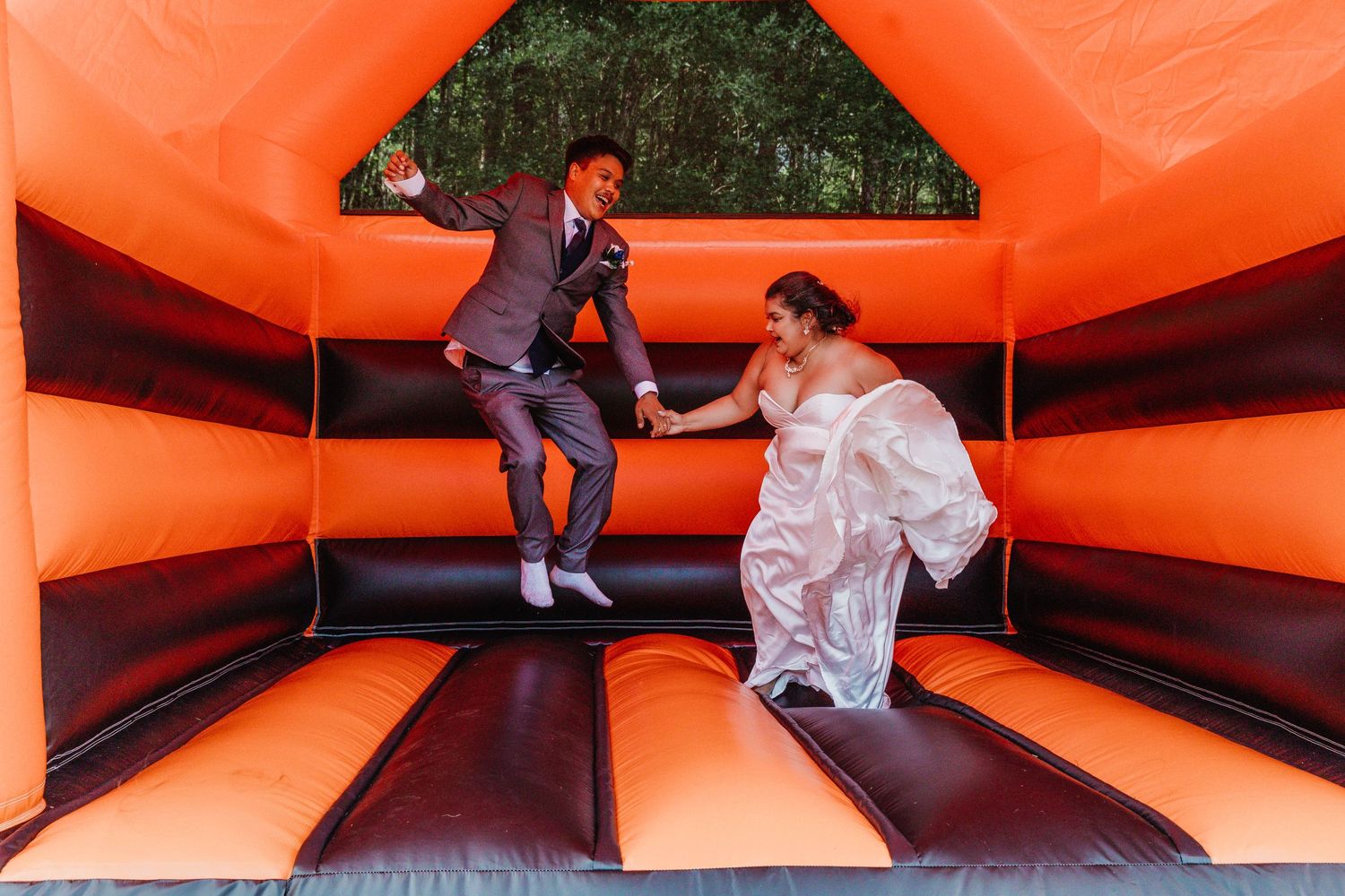 Wedding guests having fun jumping inside a bright orange bounce house.
