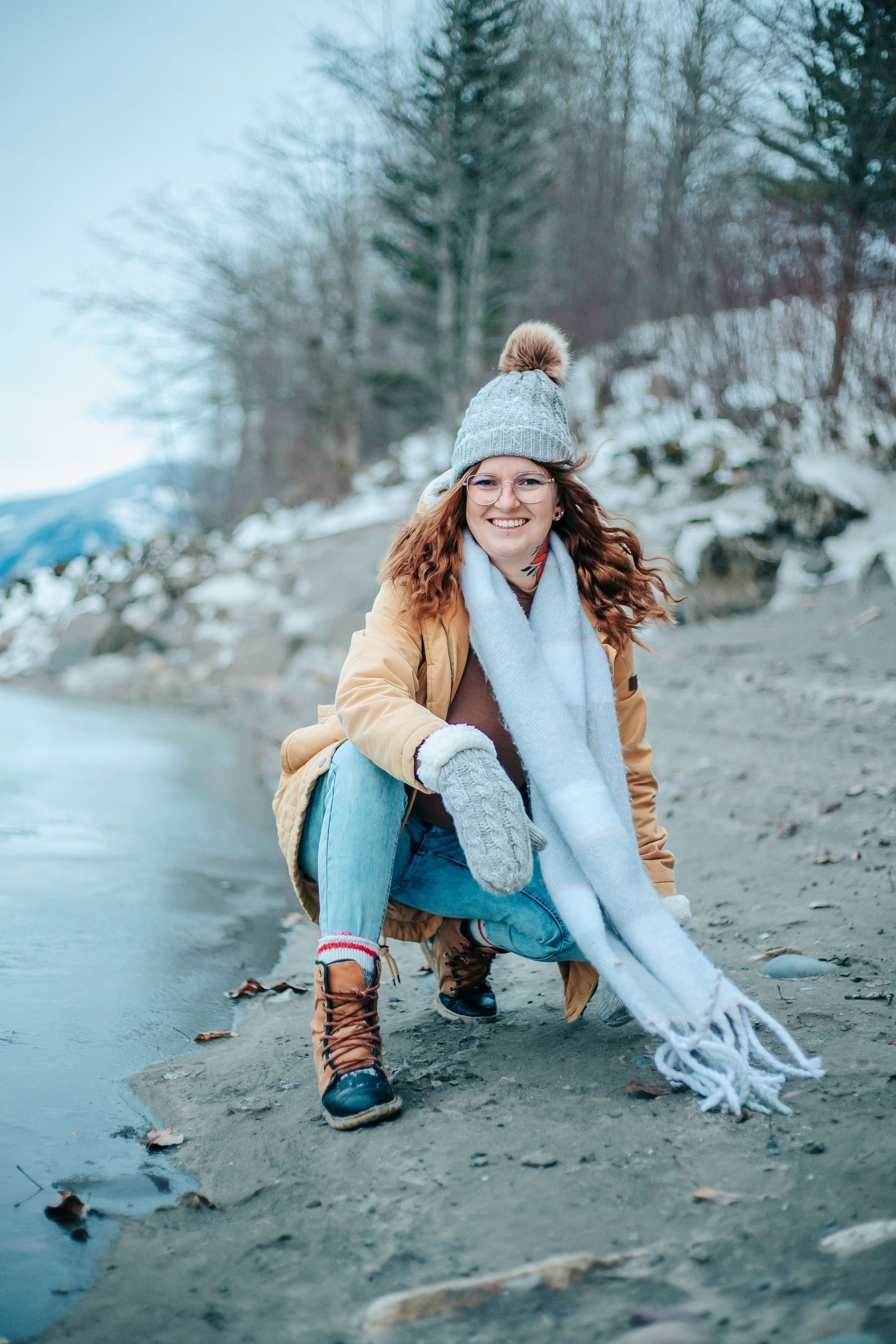 Coastal winter scene with cozy knit accessories and tan coat on rocky beach.