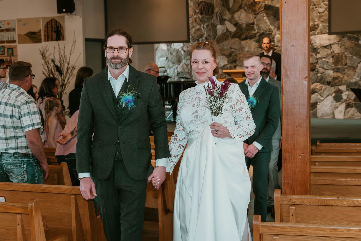 A wedding party walks down the church aisle between wooden pews.