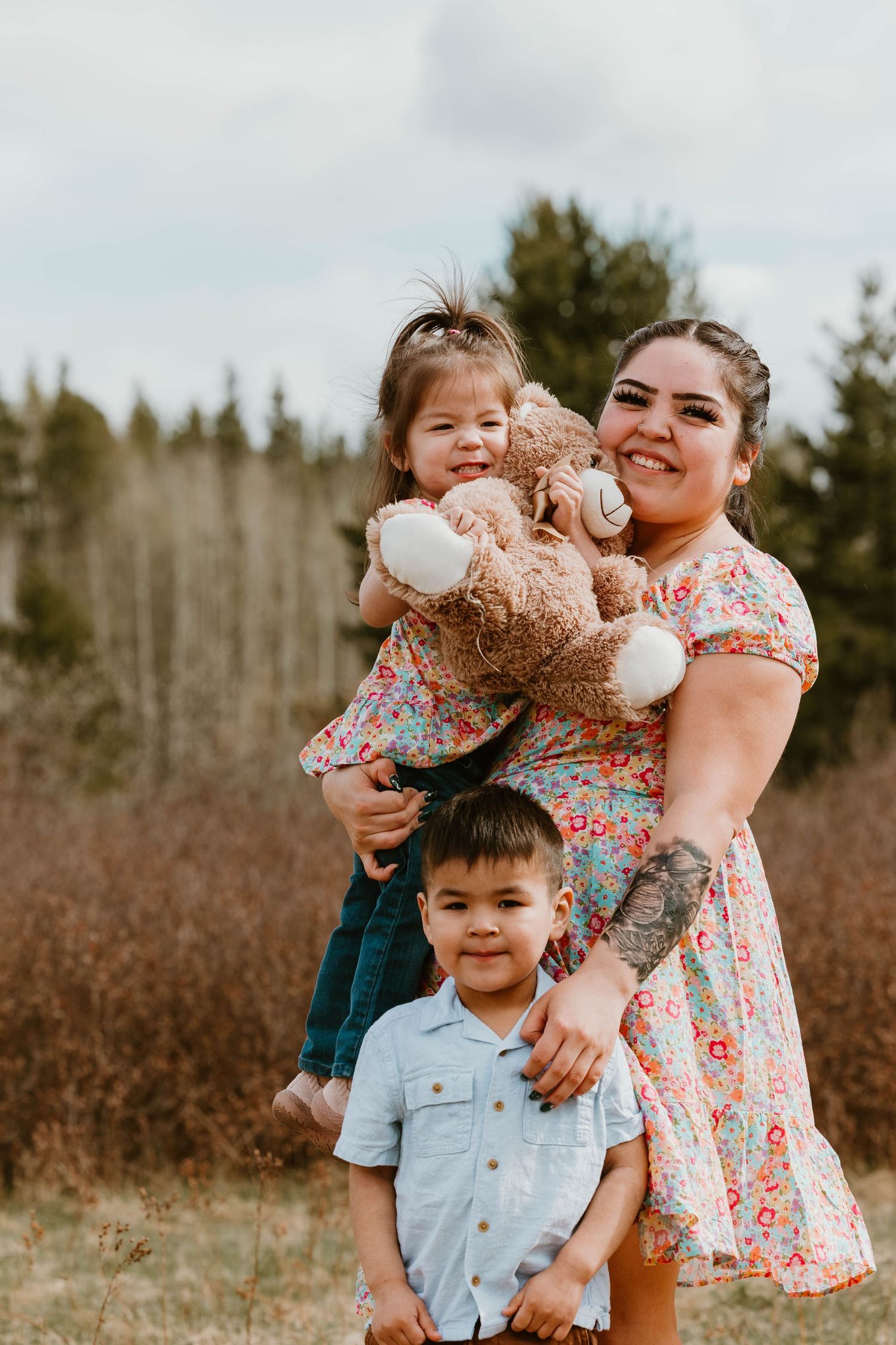 A heartwarming family portrait in nature featuring a floral dress and teddy bear.