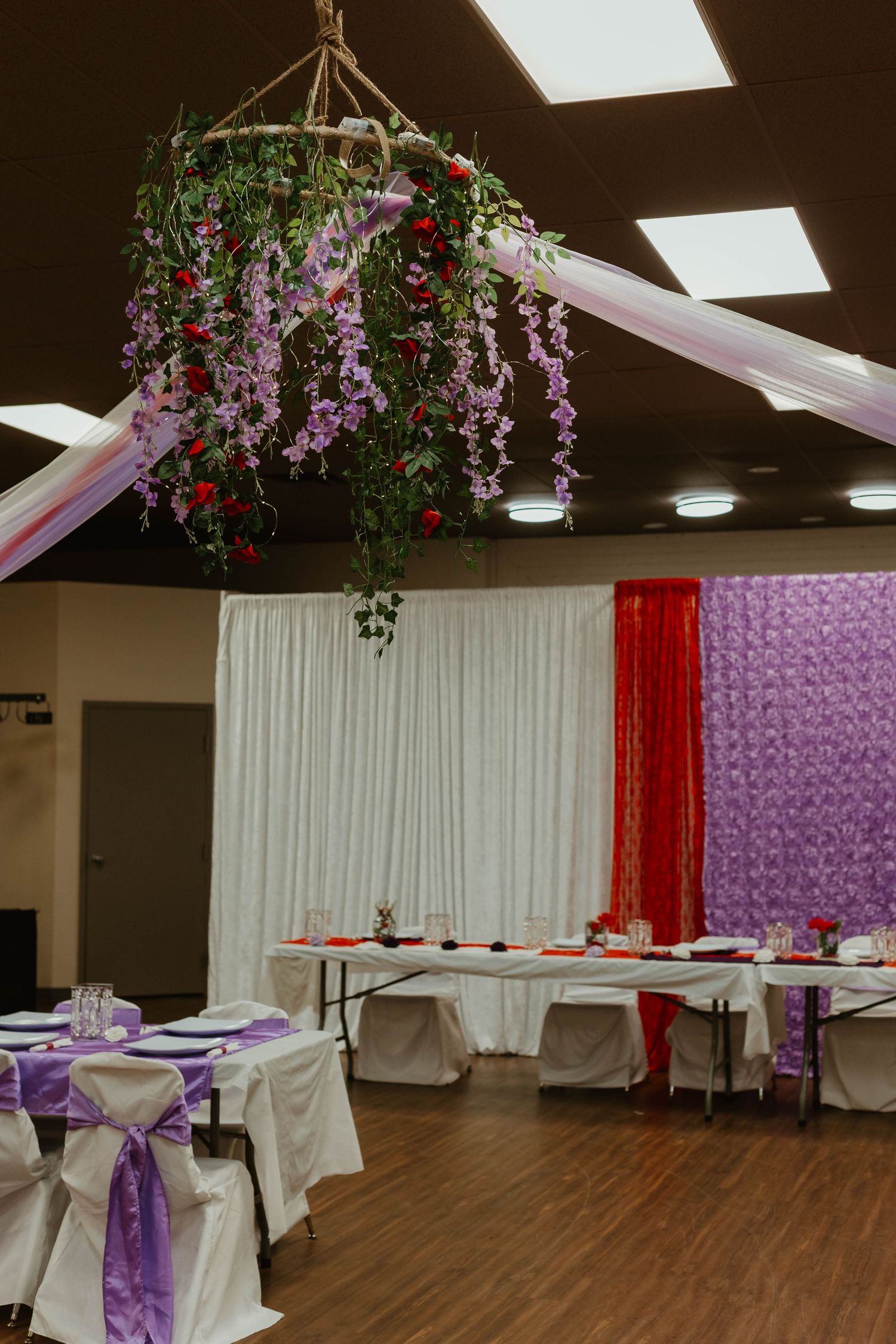 Wedding reception hall decorated with hanging floral arrangement and purple accents.