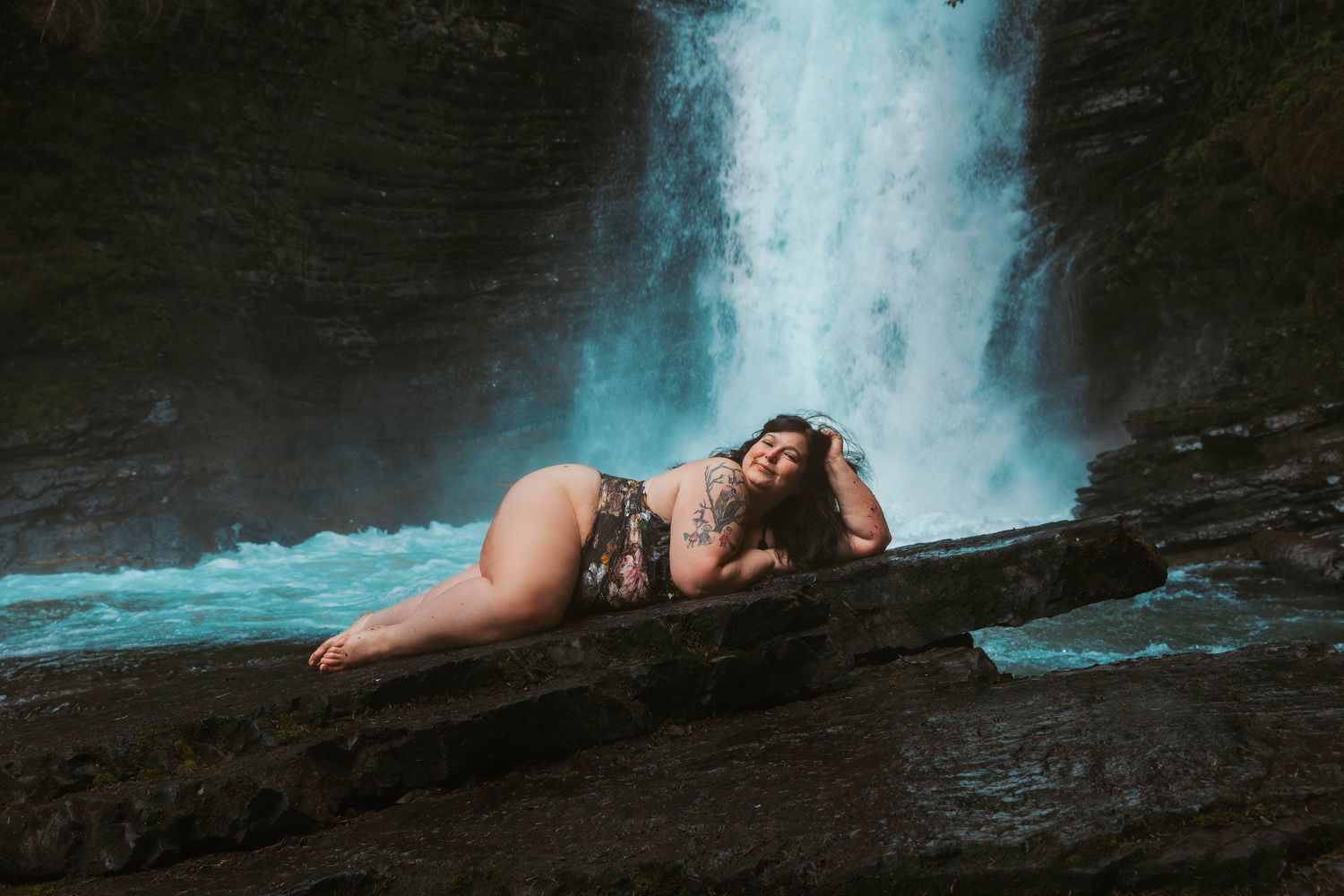 Artistic photo of person reclining on rock ledge with cascading waterfall in background.