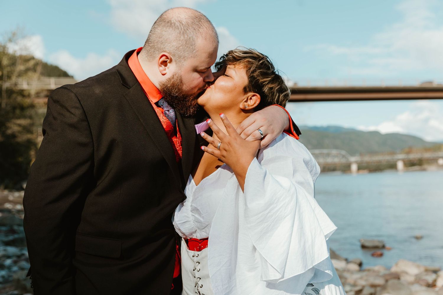 Couple shares passionate kiss against backdrop of mountains and river.
