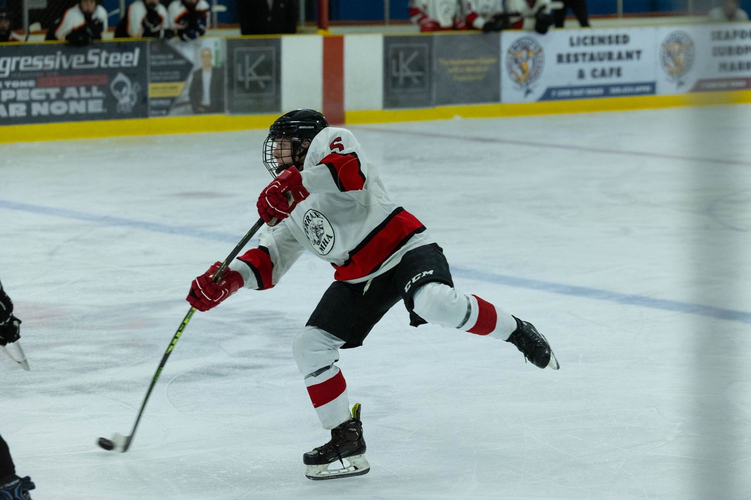 Hockey player in red and white jersey takes a shot while gliding across the ice.