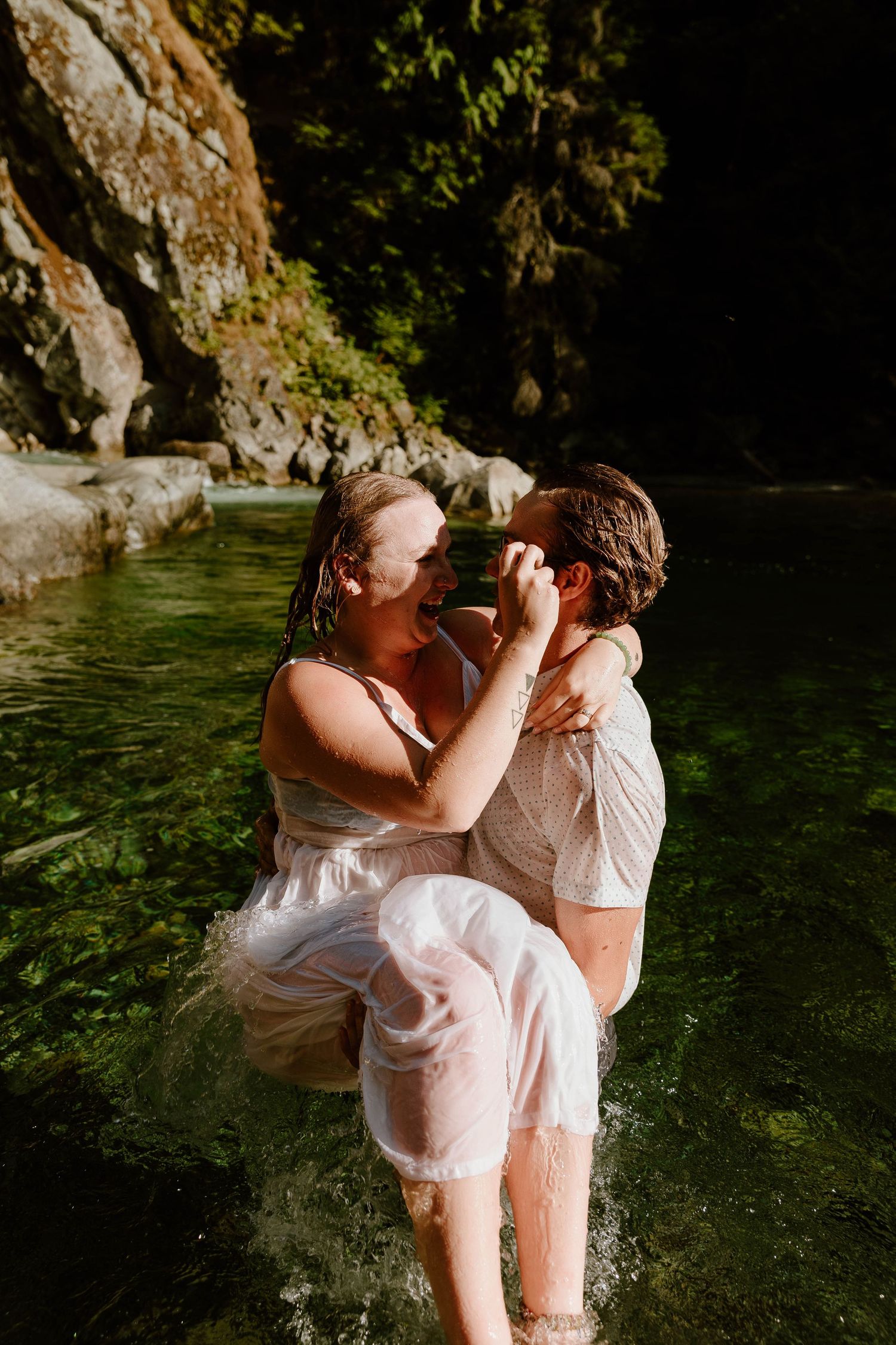 A couple in wet white clothing shares a passionate moment in mountain river water.