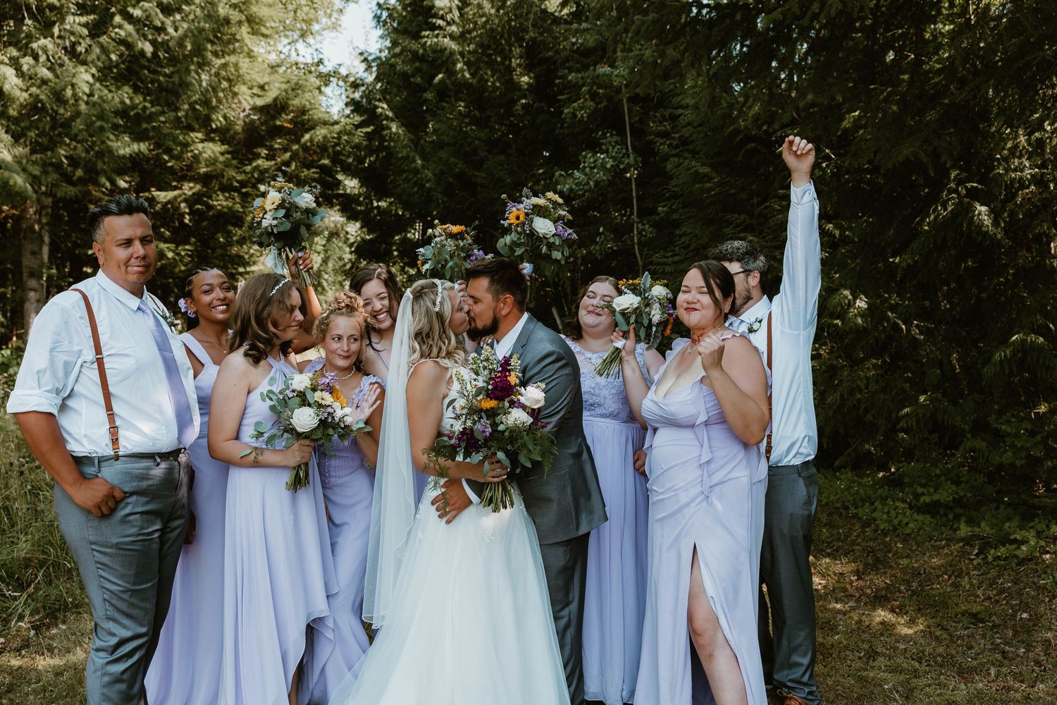 Wedding party in purple dresses and suspenders celebrating outdoors.
