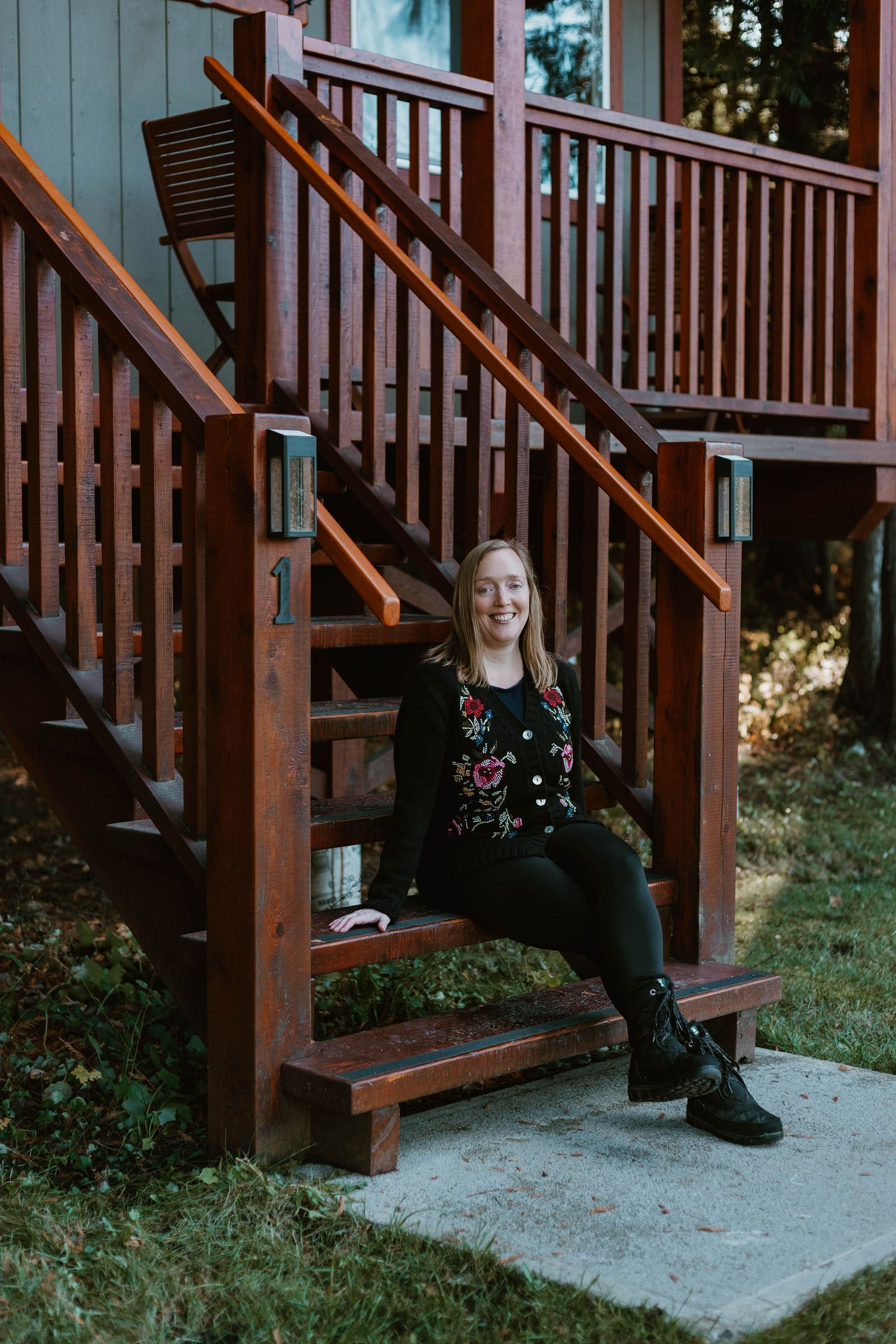 Lifestyle portrait on rustic wooden stairs with floral sweater and black boots.