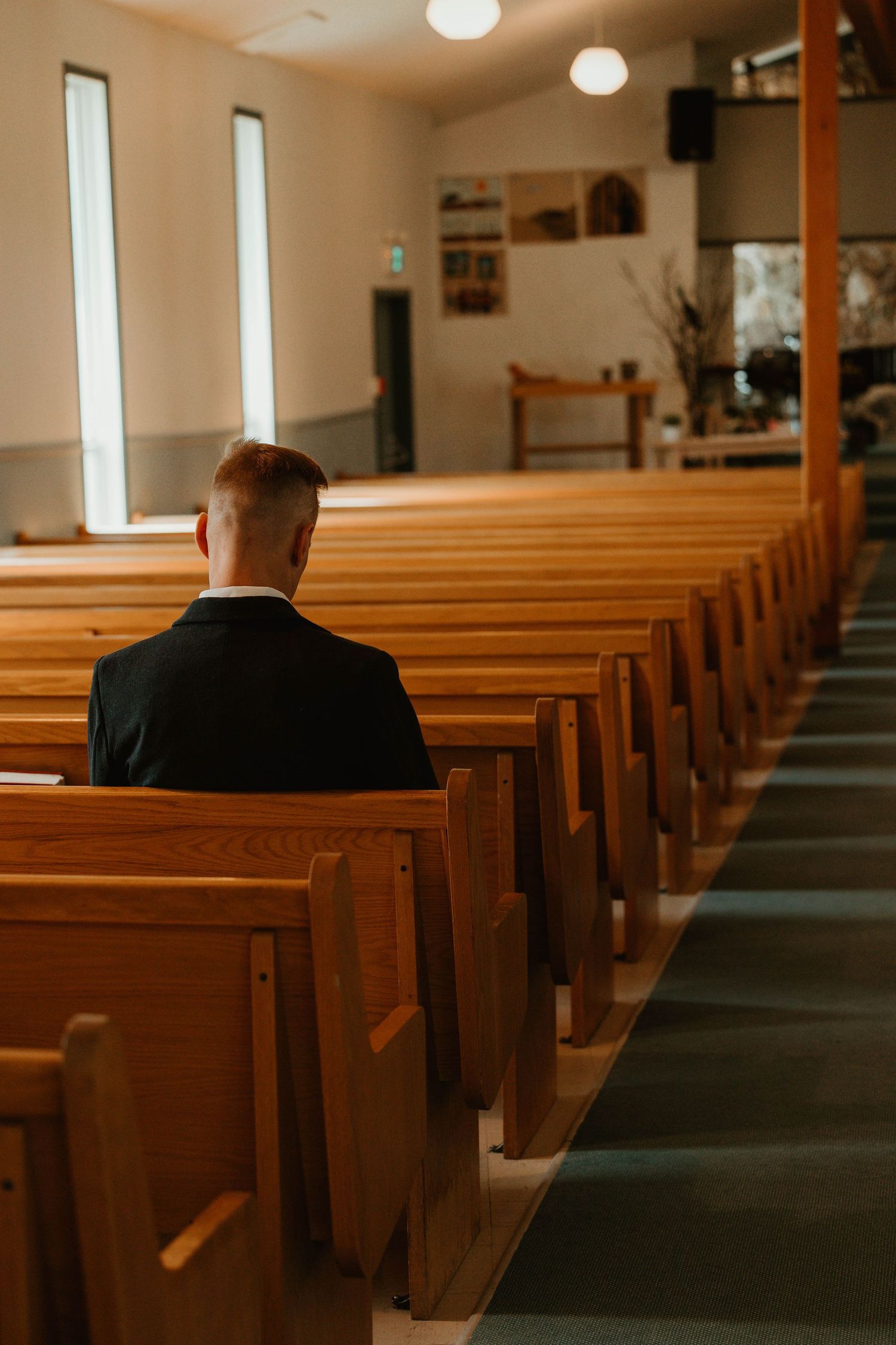 A person sitting alone in wooden church pews illuminated by warm lighting.