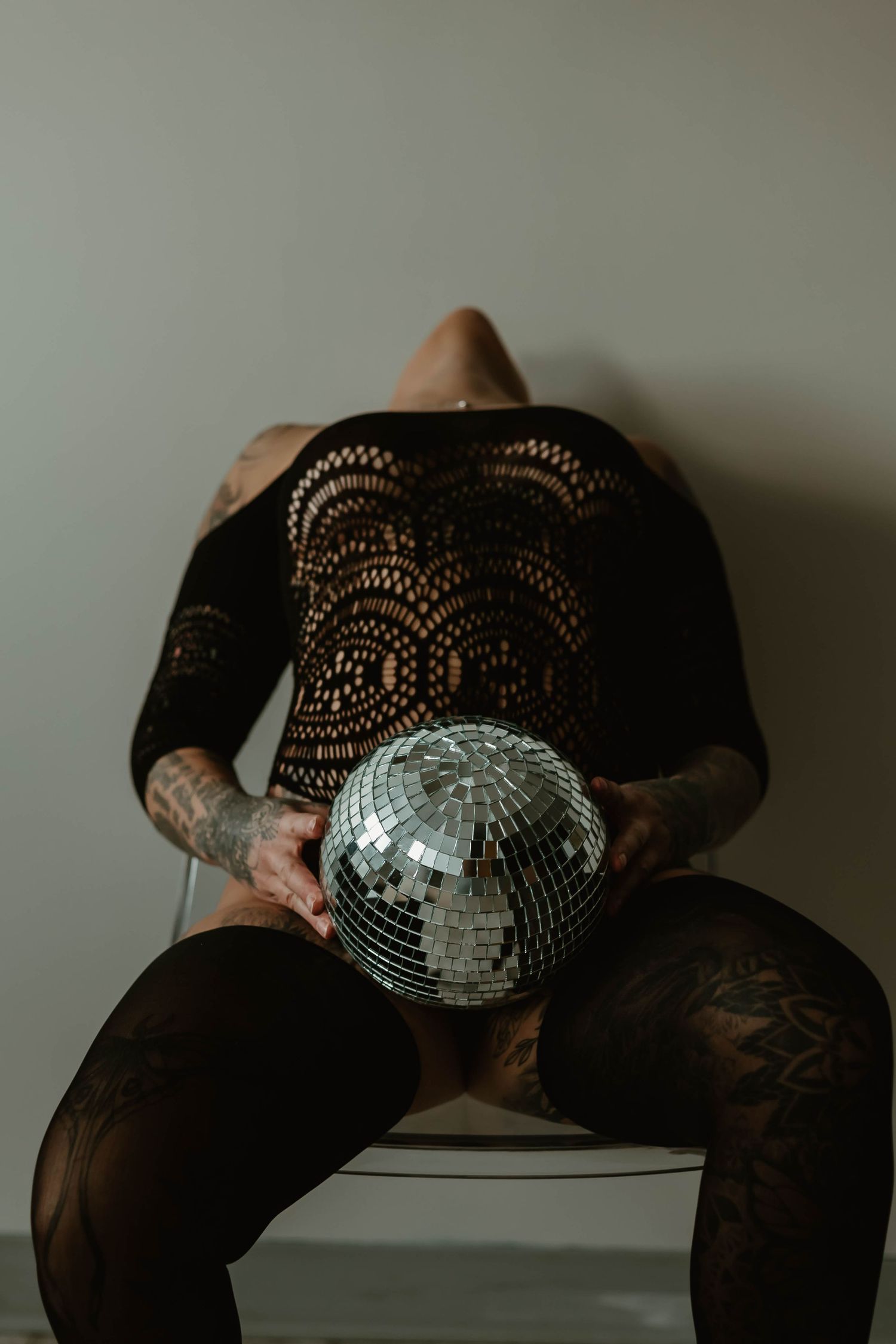 Person in black lace holding disco ball while sitting on chair.