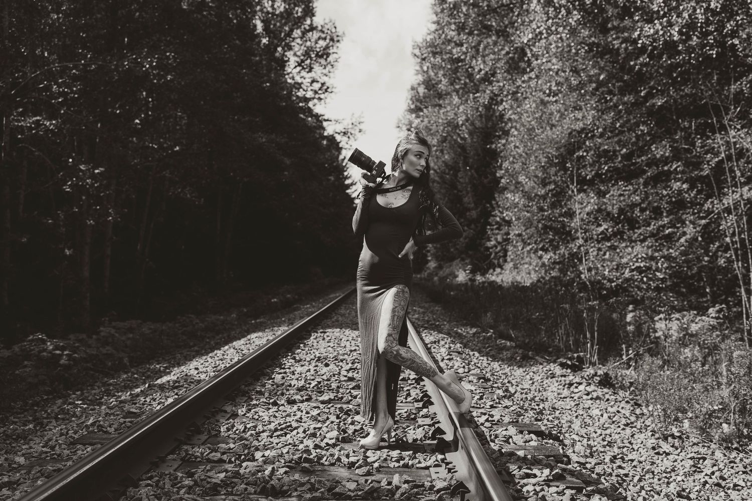 A silhouette of someone balancing on train tracks through a forest in black and white.